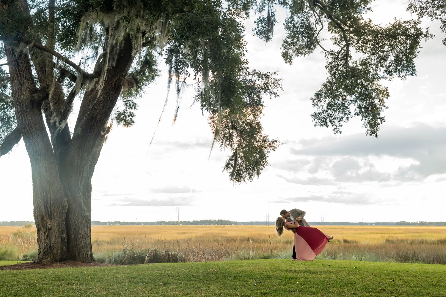 Romantic photo session in a serene field with a majestic oak tree draped in Spanish moss at sunset.