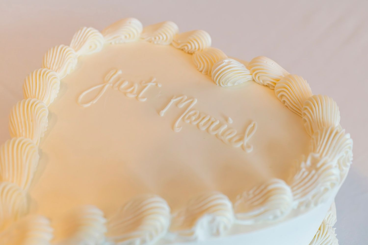 White heart-shaped cake with delicate piped frosting decoration in soft peach tones.