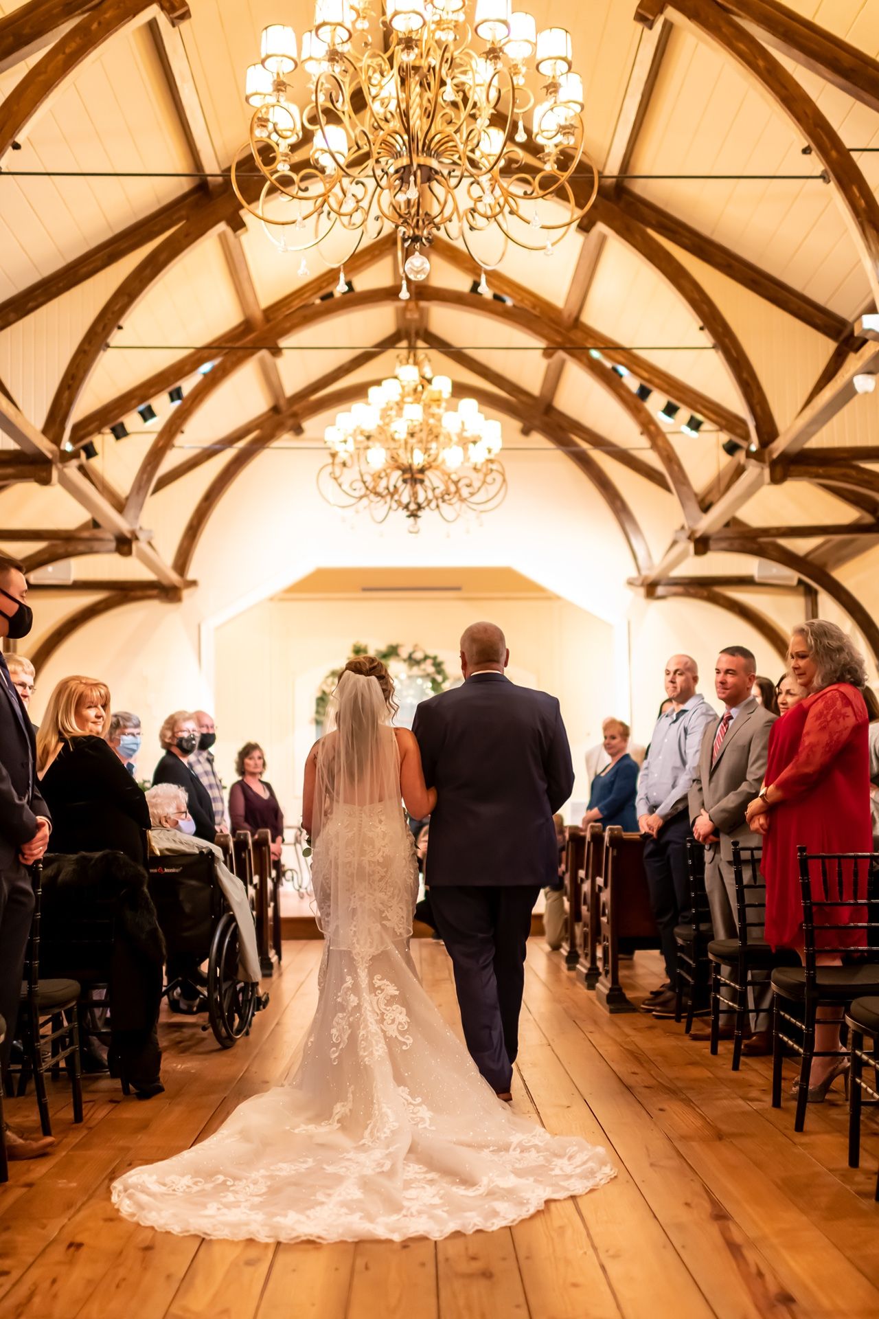 Elegant wedding ceremony in a vaulted room with wooden beams and crystal chandeliers.