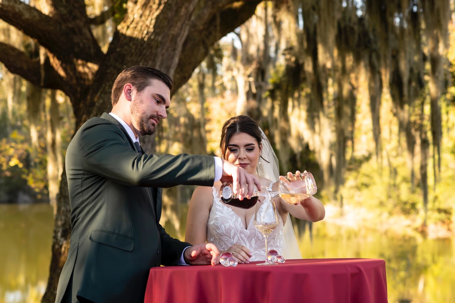 A couple performs a unity ceremony at an outdoor wedding with Spanish moss hanging from trees in the background.