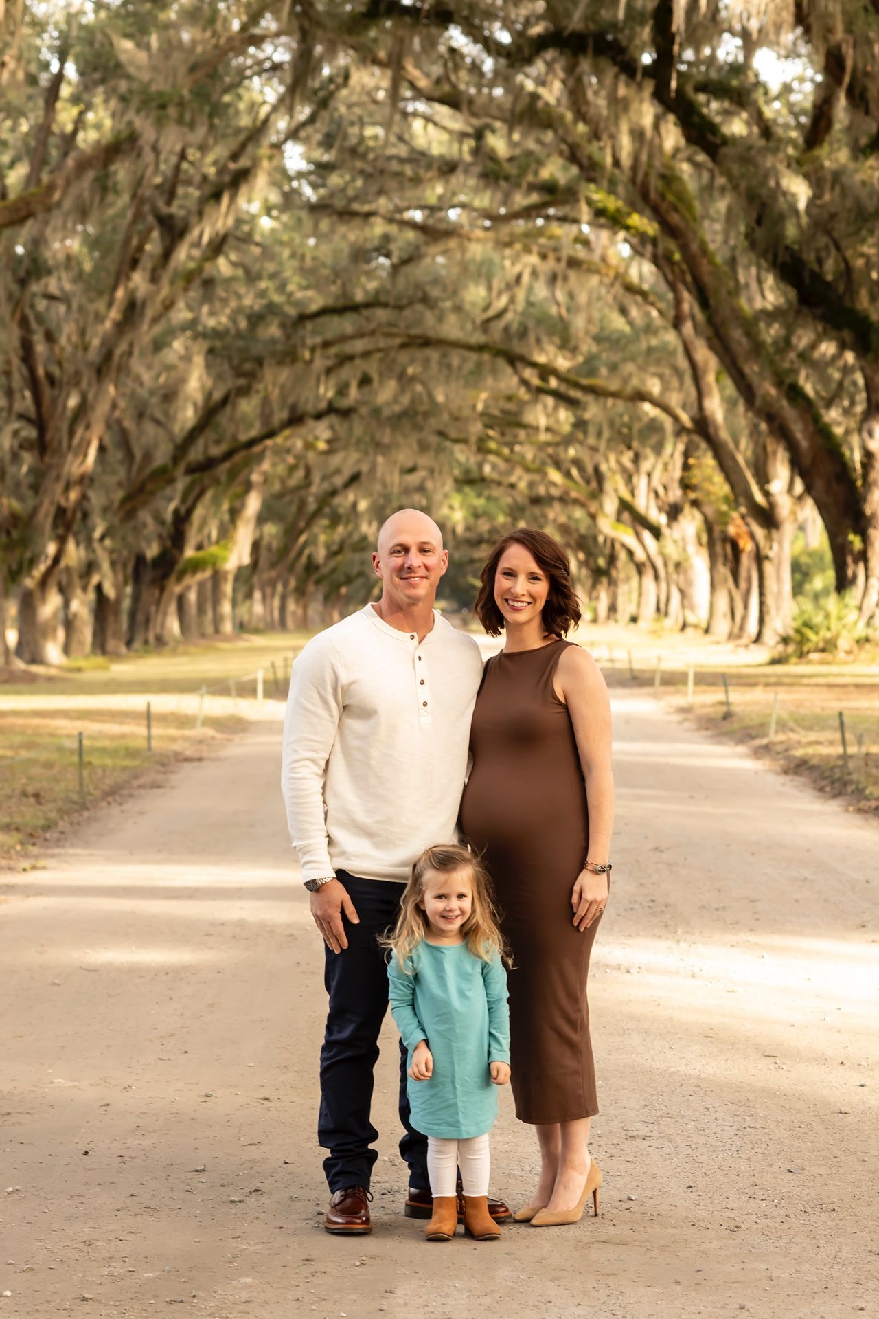Family stands on a dirt path beneath a beautiful canopy of oak trees draped in Spanish moss.