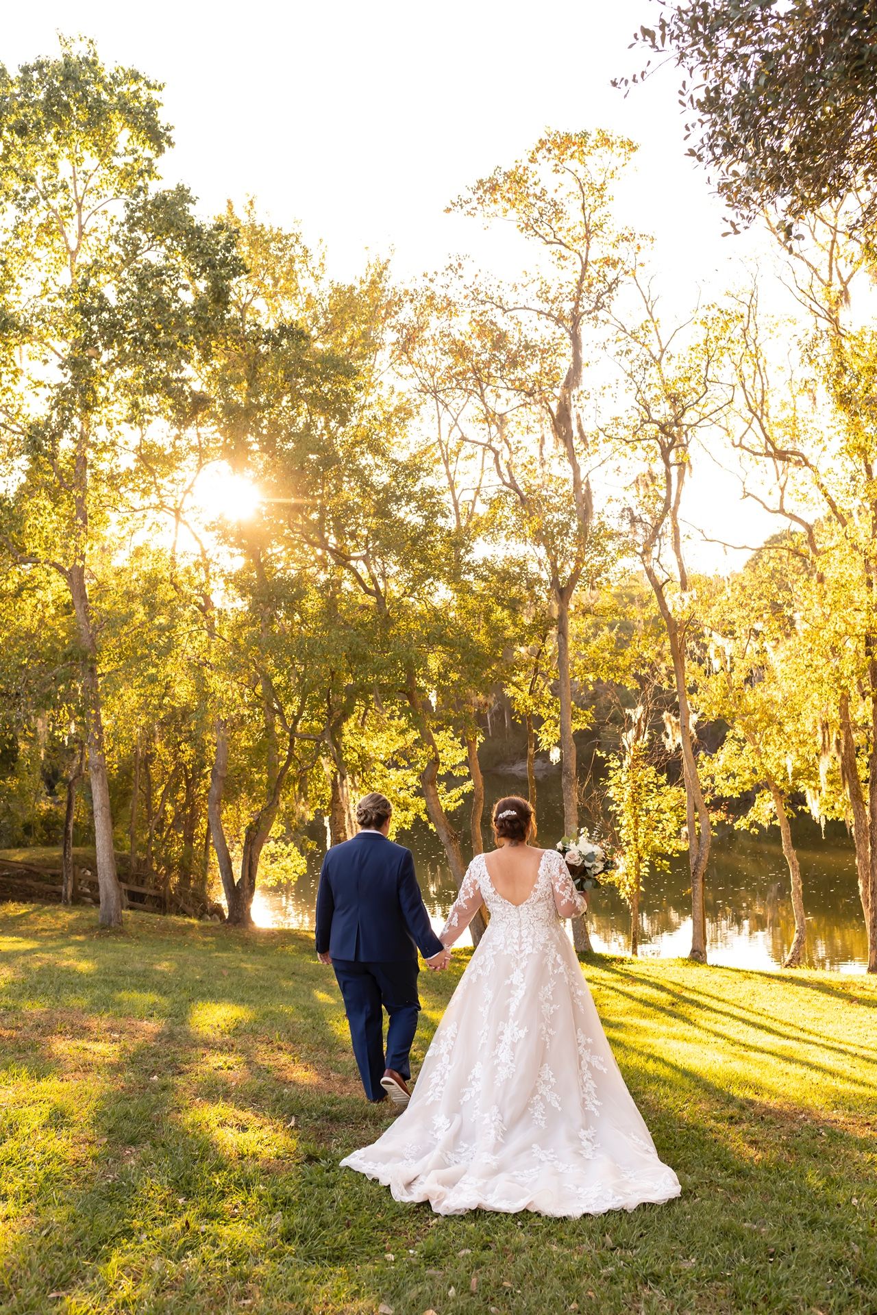 A newlywed couple walks hand in hand through a sun-drenched meadow during golden hour creating a romantic silhouette.