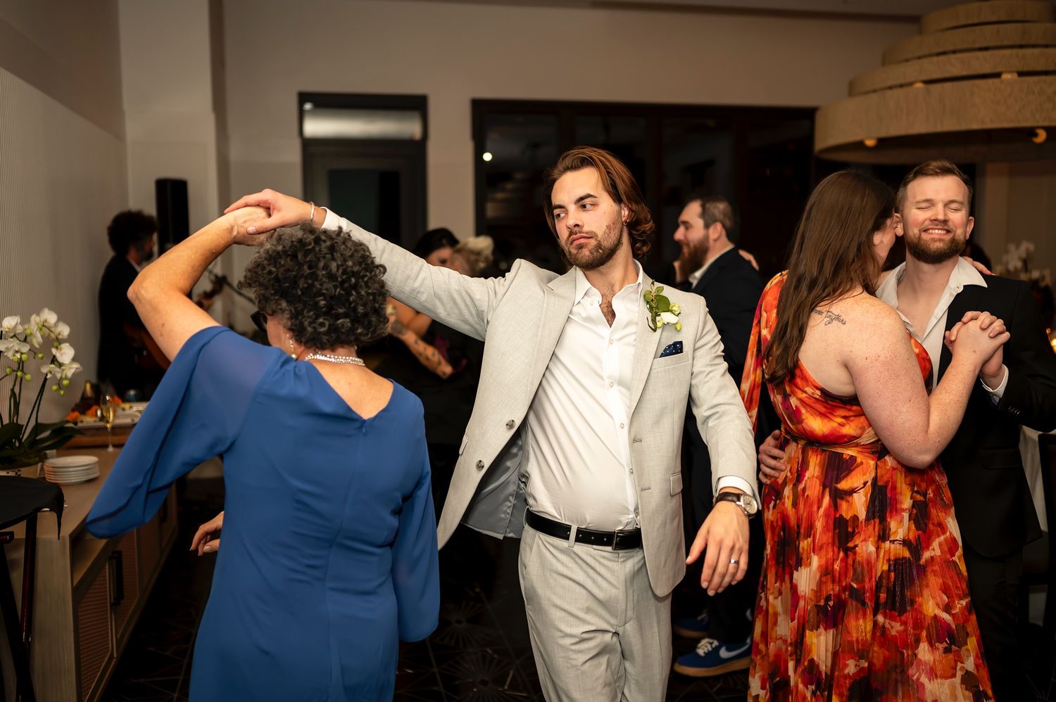 A group of party guests dancing and mingling on a crowded dance floor at an indoor event space.