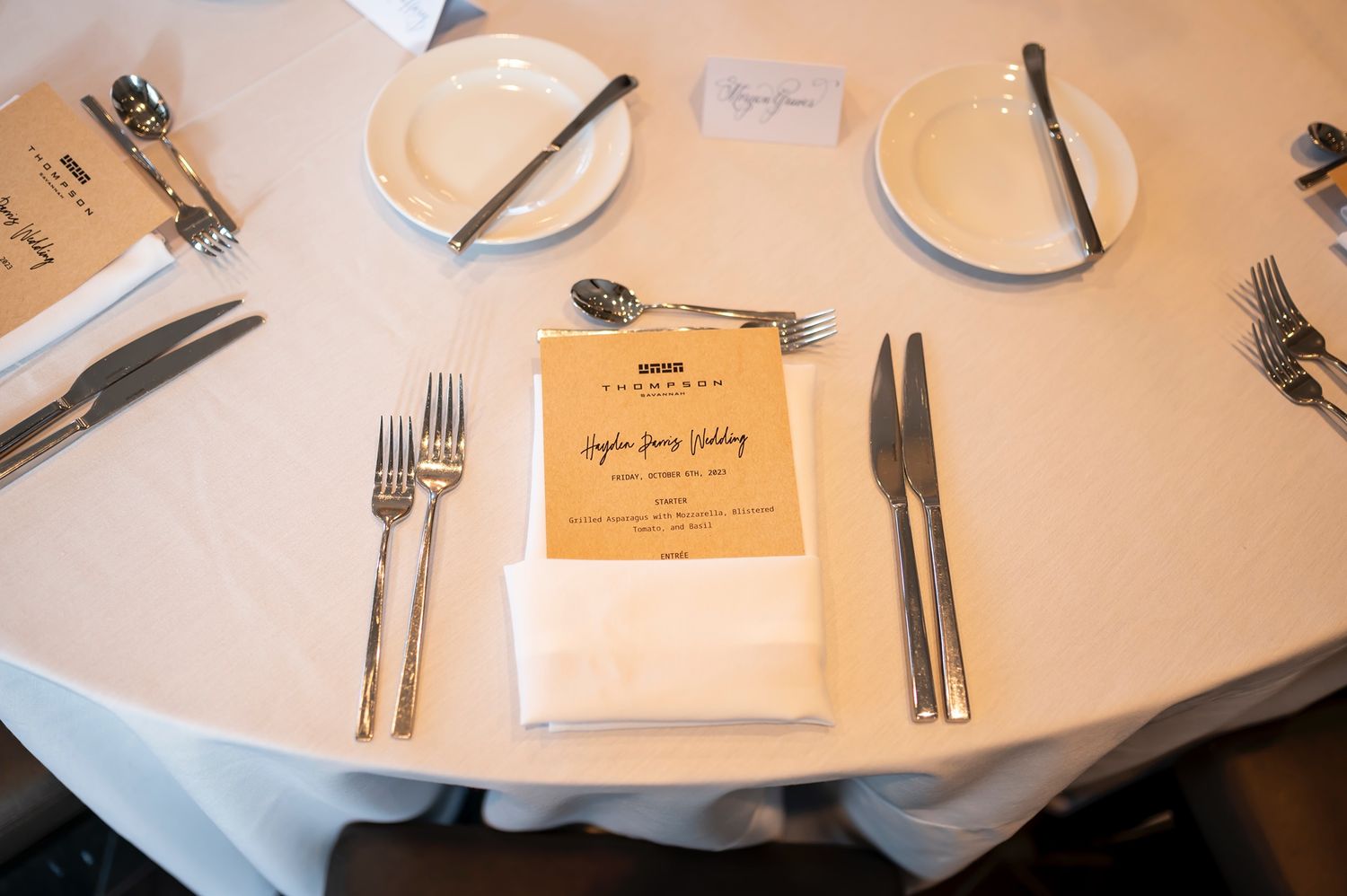 A set table at a restaurant with neatly arranged white plates, silverware, and menus on a white tablecloth.