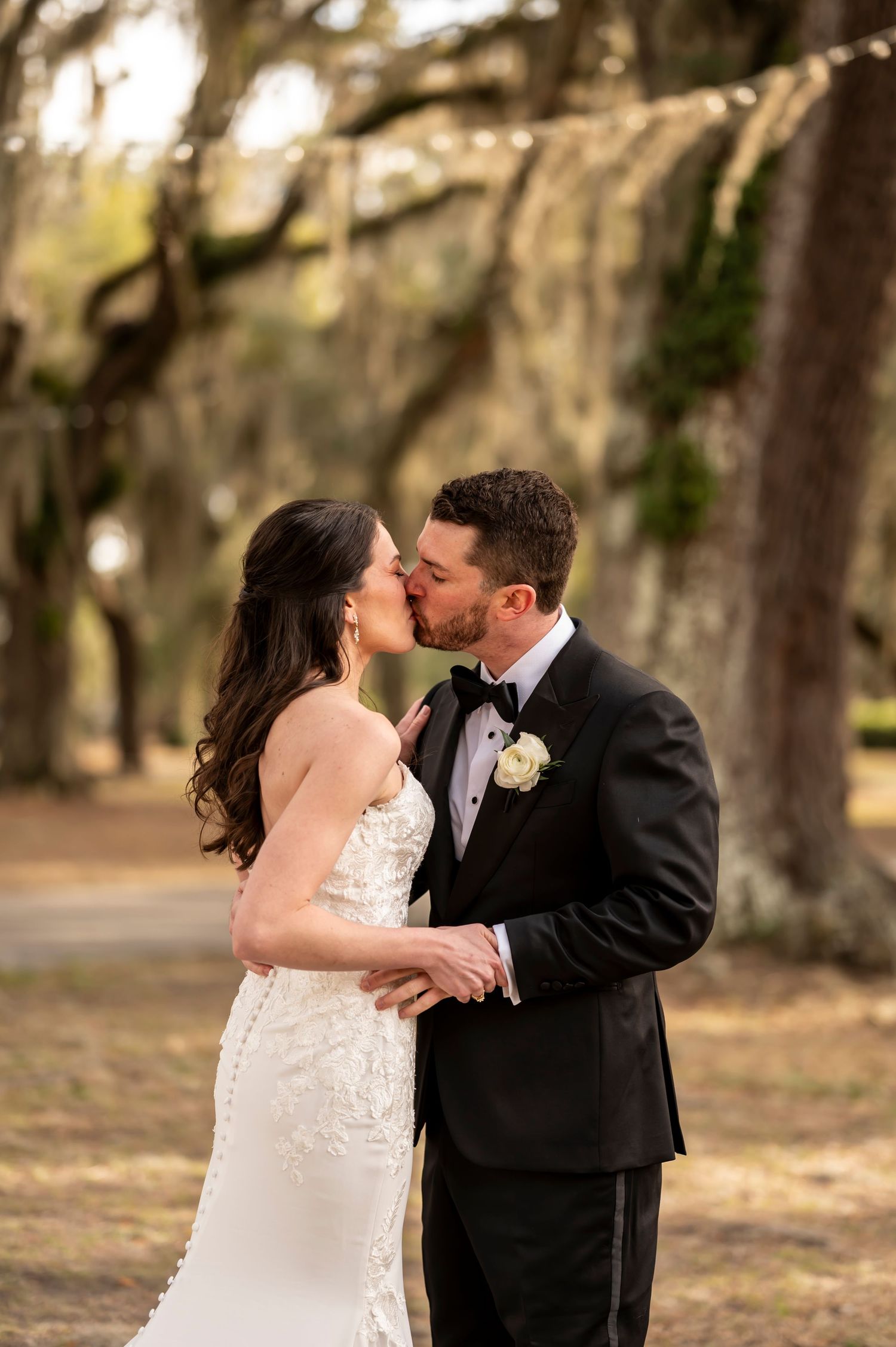 A romantic moment between newlyweds sharing a kiss under moss-draped trees in a Southern garden setting.