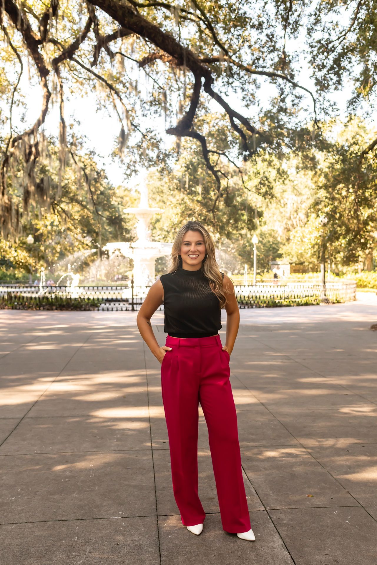 A person wearing a black sleeveless top and vibrant red wide-leg pants poses outdoors under Spanish moss draped trees.