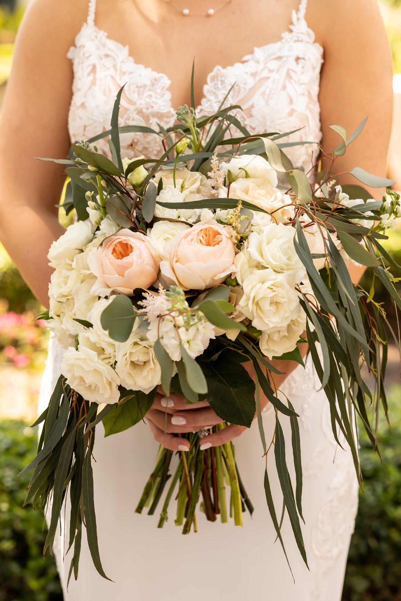 Four delicate wedding bouquets with peach and white roses, eucalyptus leaves, and trailing greenery held against white dresses.