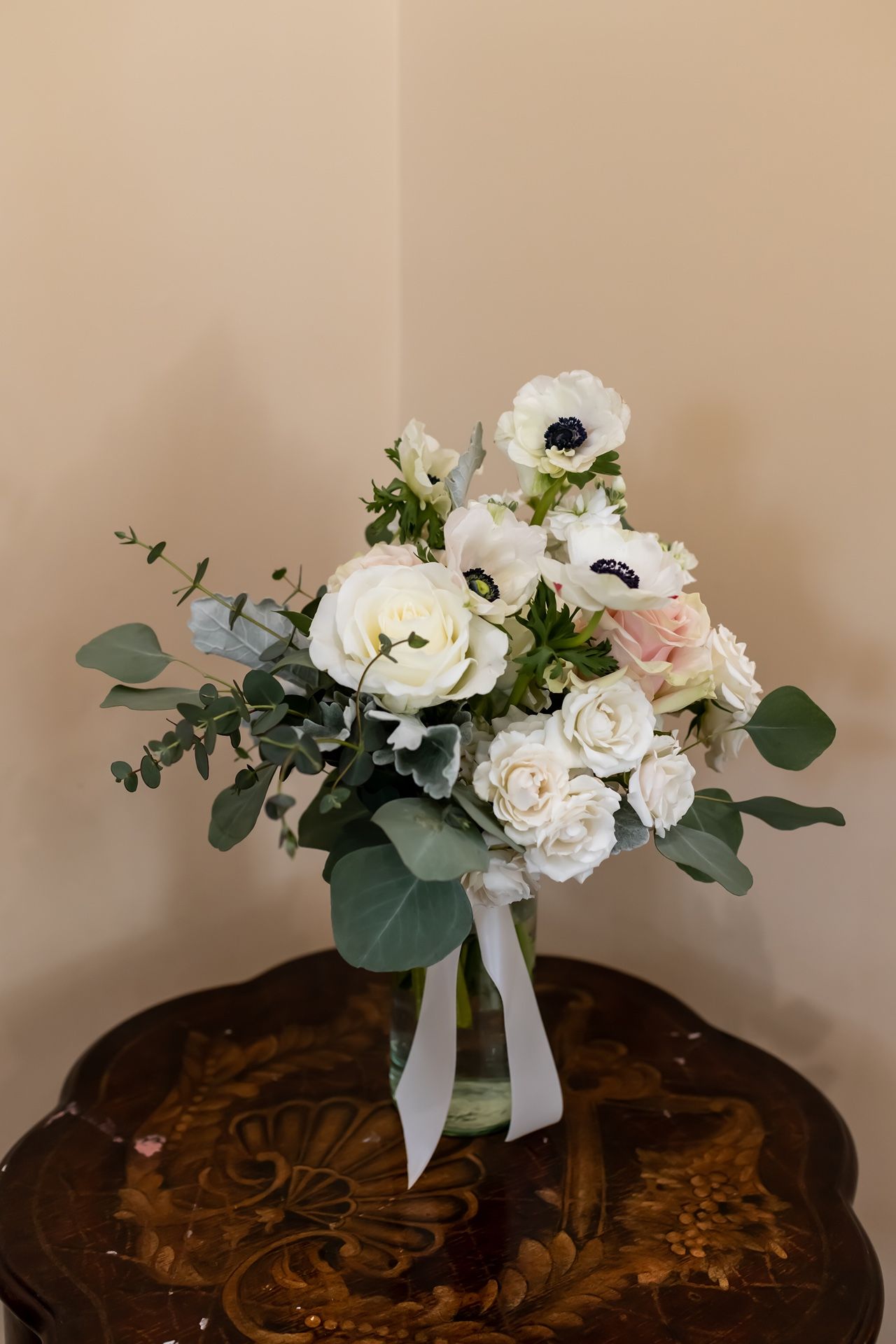 Wedding bouquet of white and pink roses with eucalyptus leaves shown from multiple angles on a dark wooden surface.