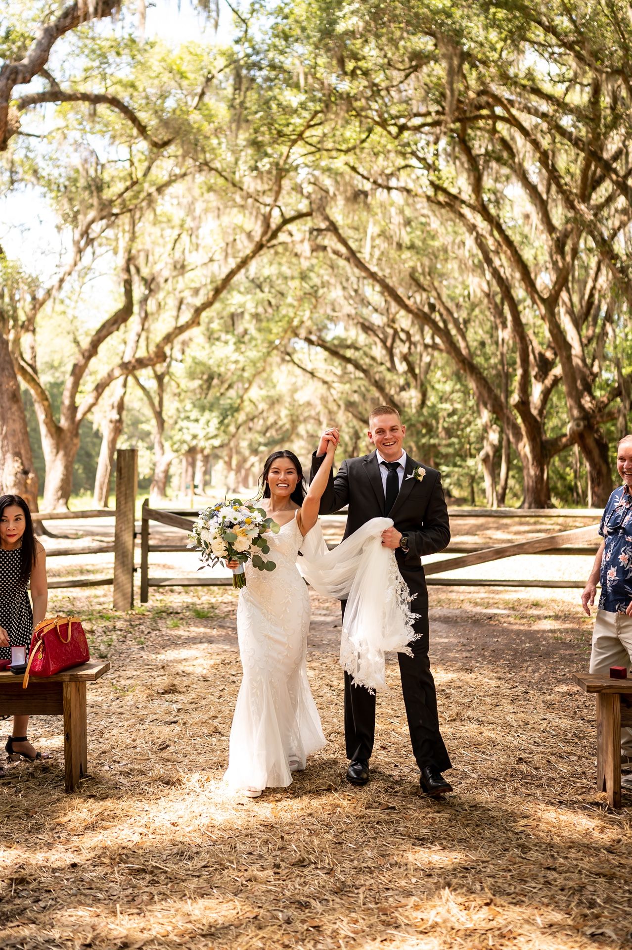 A celebration taking place in a scenic wooded area with oak trees and dappled sunlight filtering through the branches.
