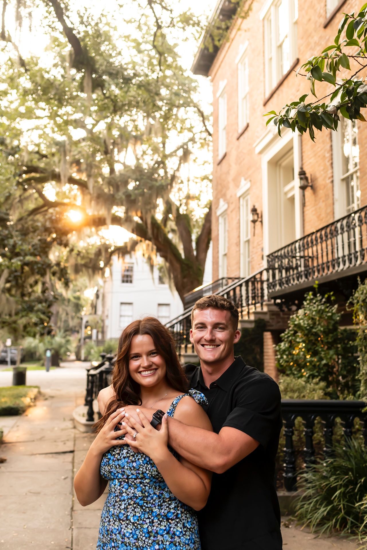 Happy couple embraces on a historic Charleston street with Spanish moss and brick buildings at sunset.