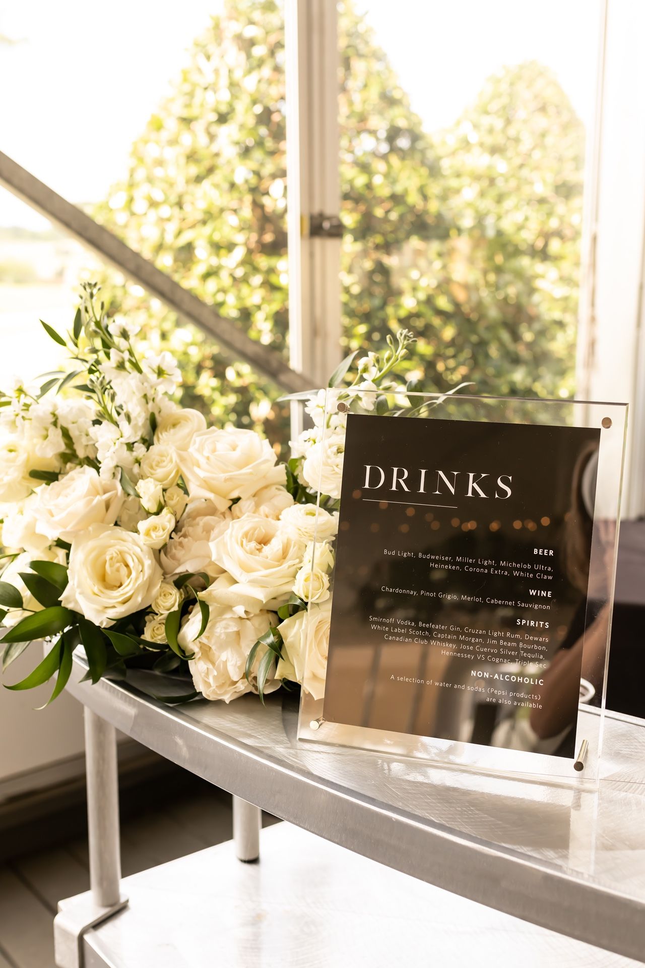 White floral arrangements and drink menu displays on windowsills create an elegant wedding reception atmosphere.
