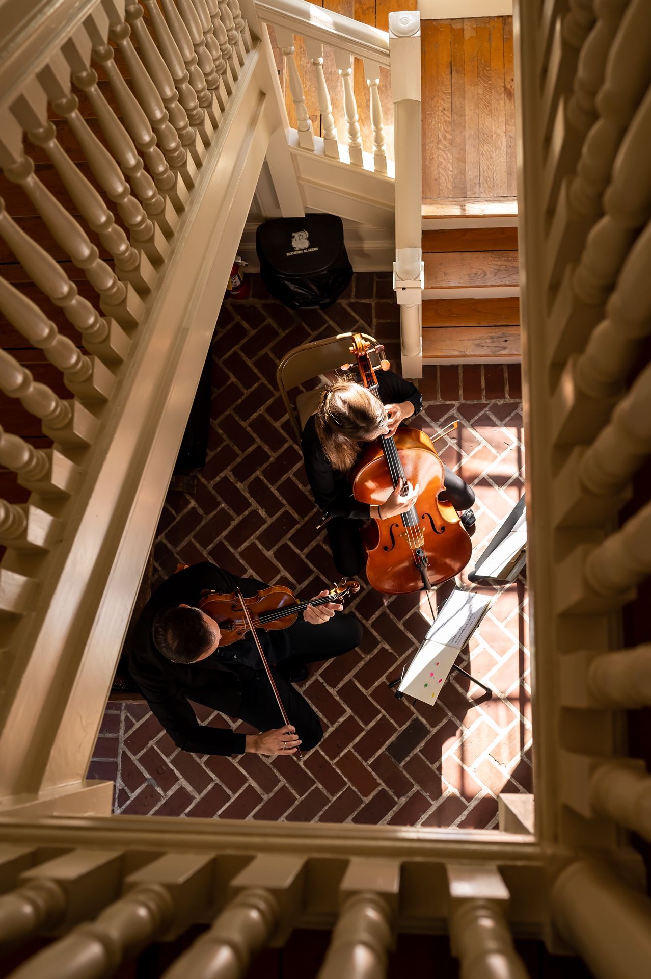 Musicians performing classical music on string instruments viewed from above through a stairwell with wooden railings.