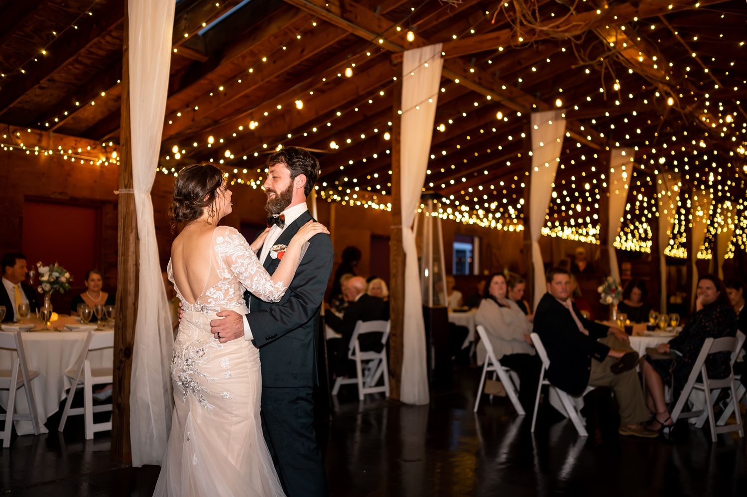 Elegant wedding reception venue decorated with twinkling lights and glowing candles as couple shares first dance.