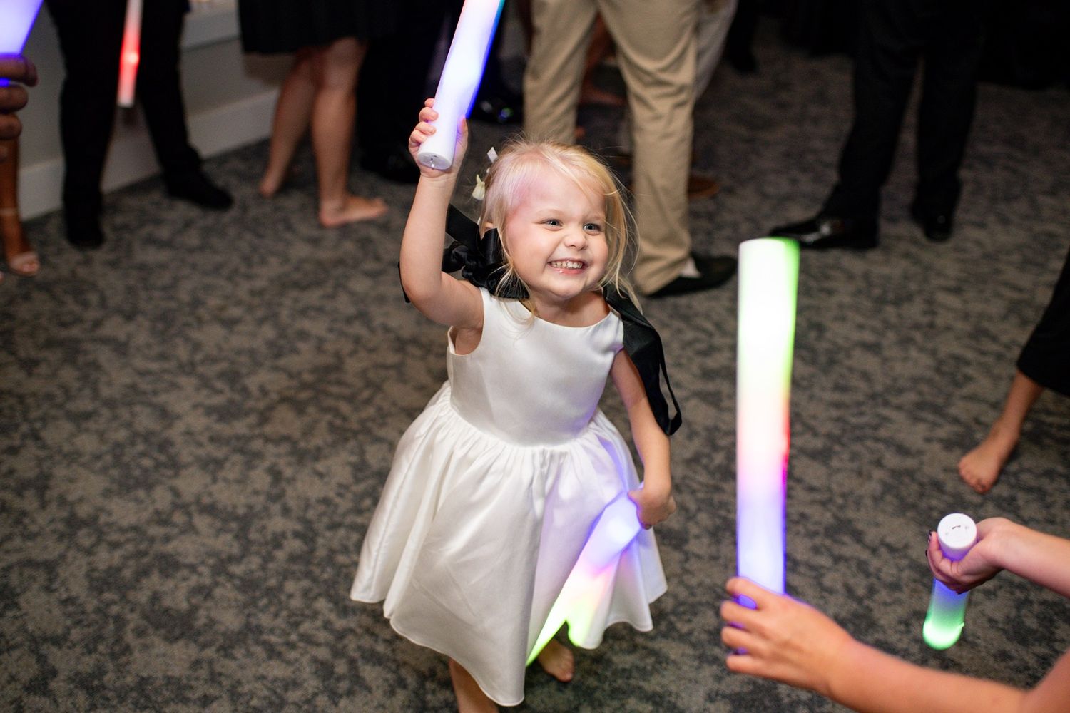 Children play with colorful light-up wands on a carpeted dance floor at a wedding reception.