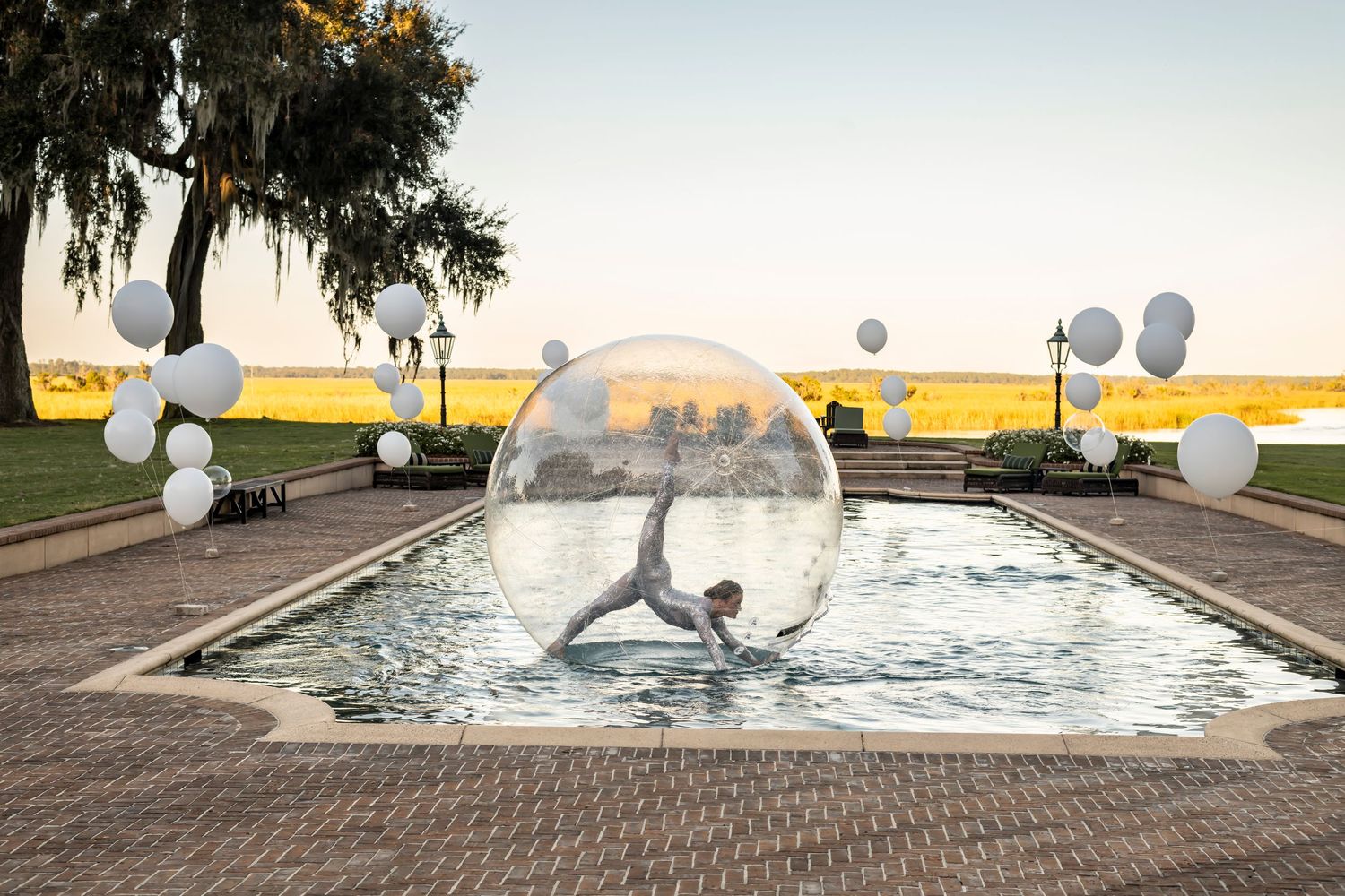 An acrobat at a corporate event with white balloons decorating outdoor celebration space at sunset.