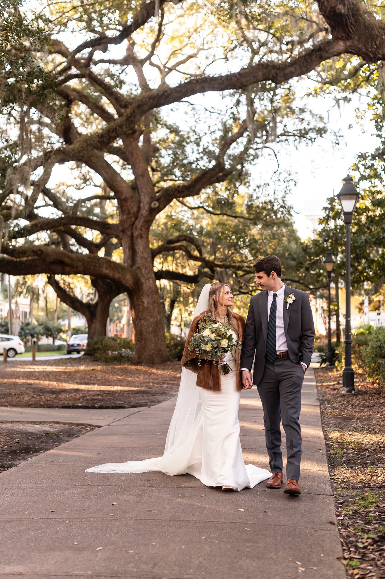 A couple shares intimate moments beneath majestic oak trees during sunset in a park setting.