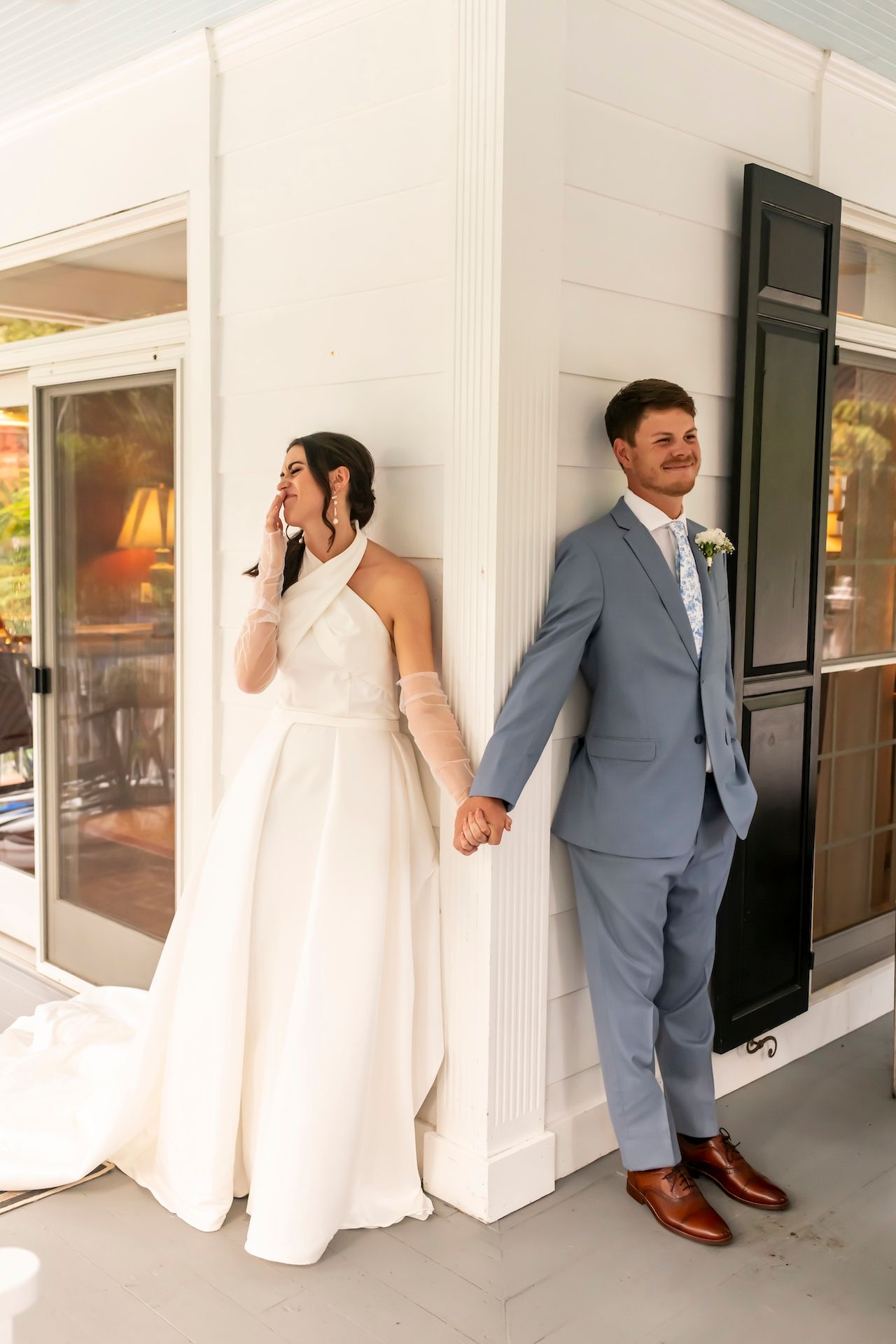 A bride and groom share a private moment around a corner before their wedding ceremony in an elegant white hallway.