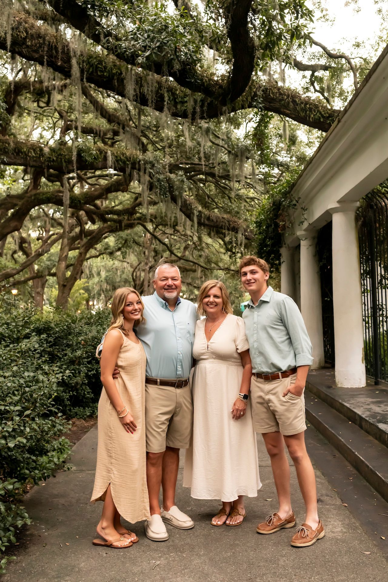 A group poses under Spanish moss-draped trees and white columns in a Southern garden setting.