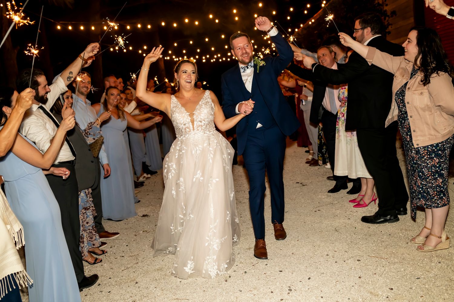Wedding guests dance together under string lights at an outdoor evening reception celebration.