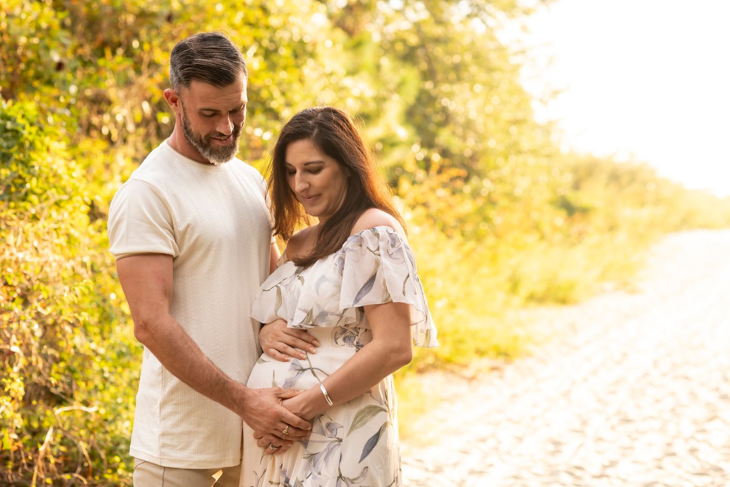Two people embrace on a sunlit path surrounded by golden foliage during sunset.