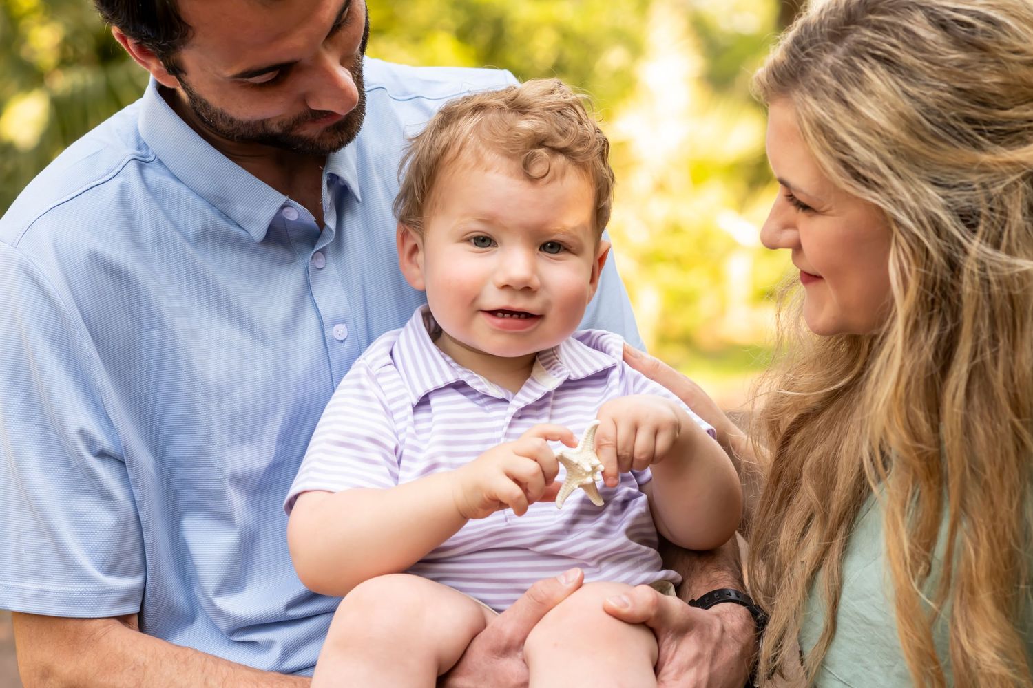 A family enjoys a tender moment together outdoors on a sunny day with golden bokeh lighting in the background.
