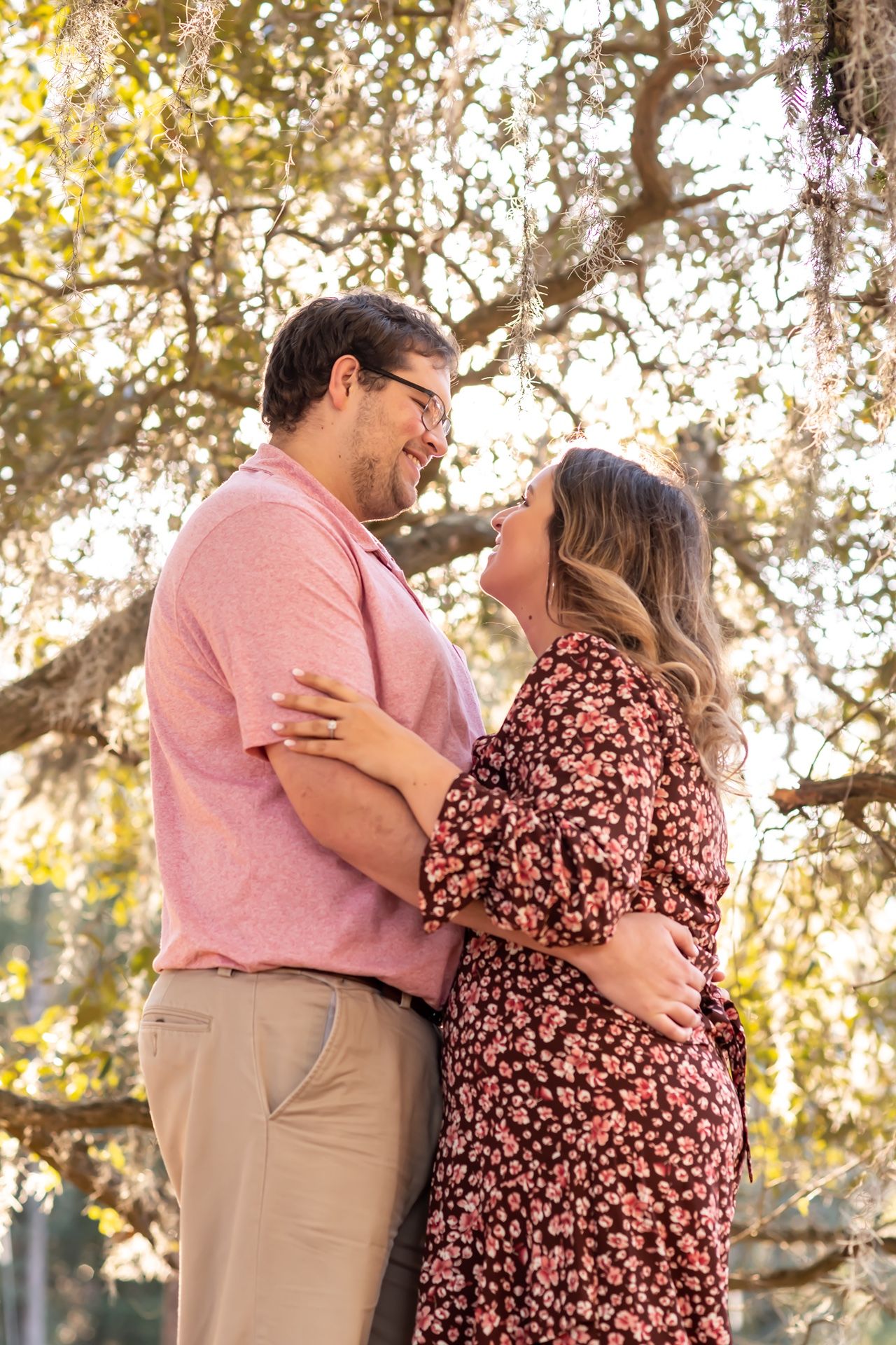 A couple shares a tender moment outdoors in golden sunlight, wearing pink and floral attire.