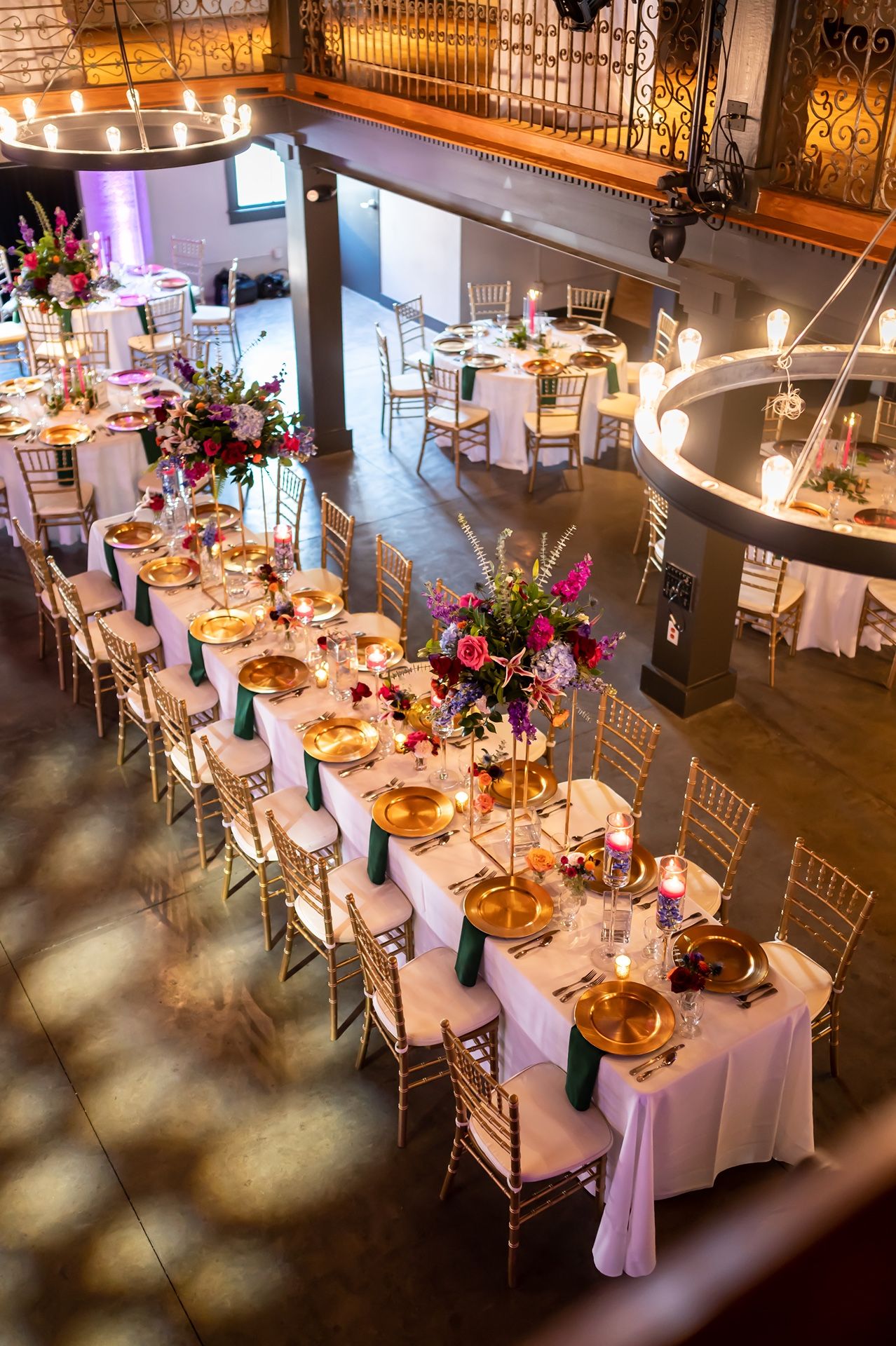 Elegant wedding reception venue with long tables set for dinner featuring white linens, gold accents, and floral centerpieces.