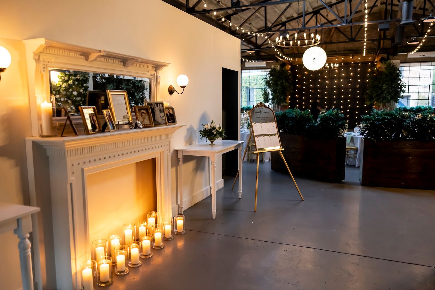 Warmly lit rustic wedding venue interior with decorative string lights and glowing candles along an elegant aisle.