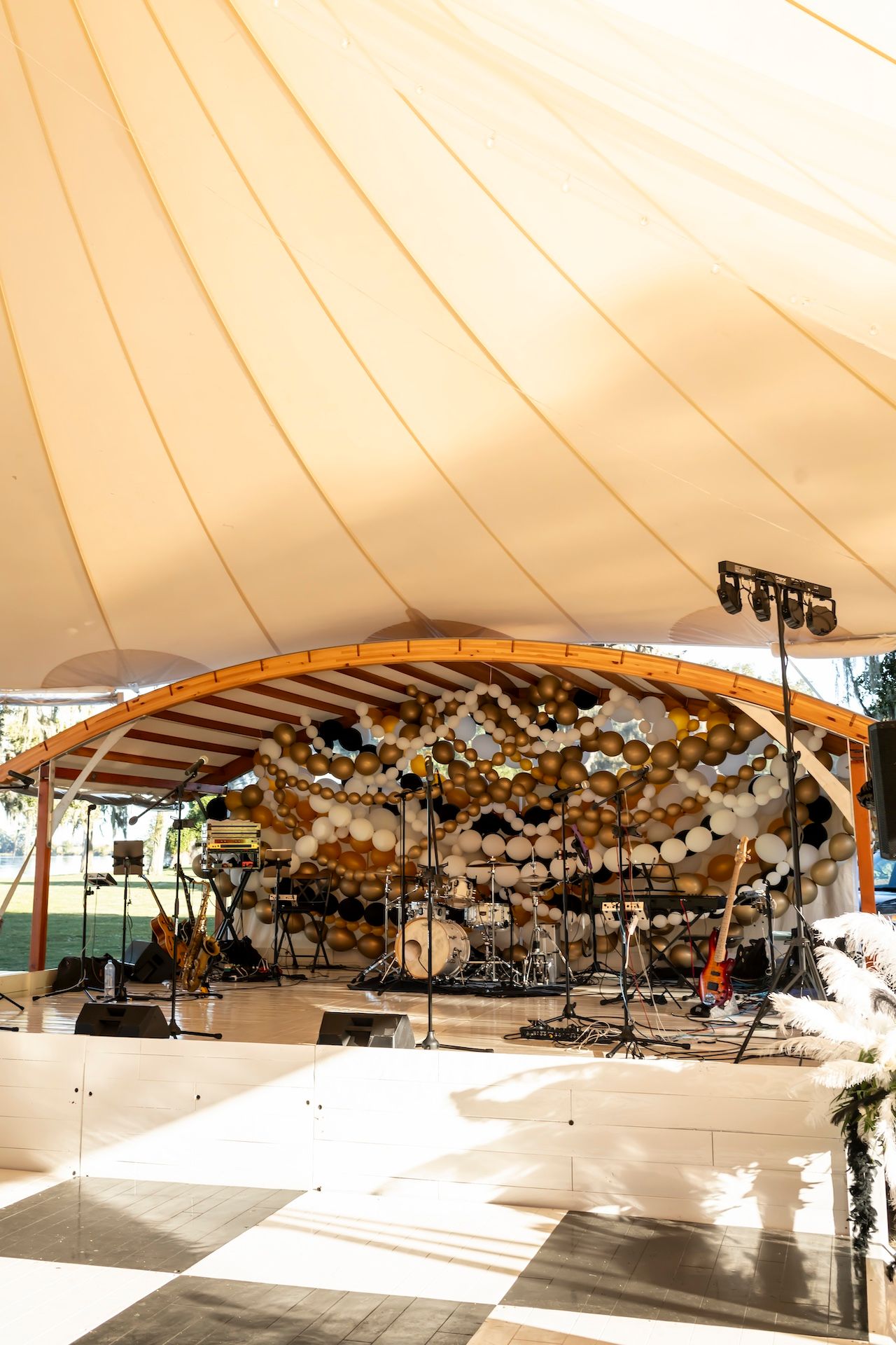 Wedding tent setup with curved wooden beams, checkered dance floor, and suspended decorative flower installations.