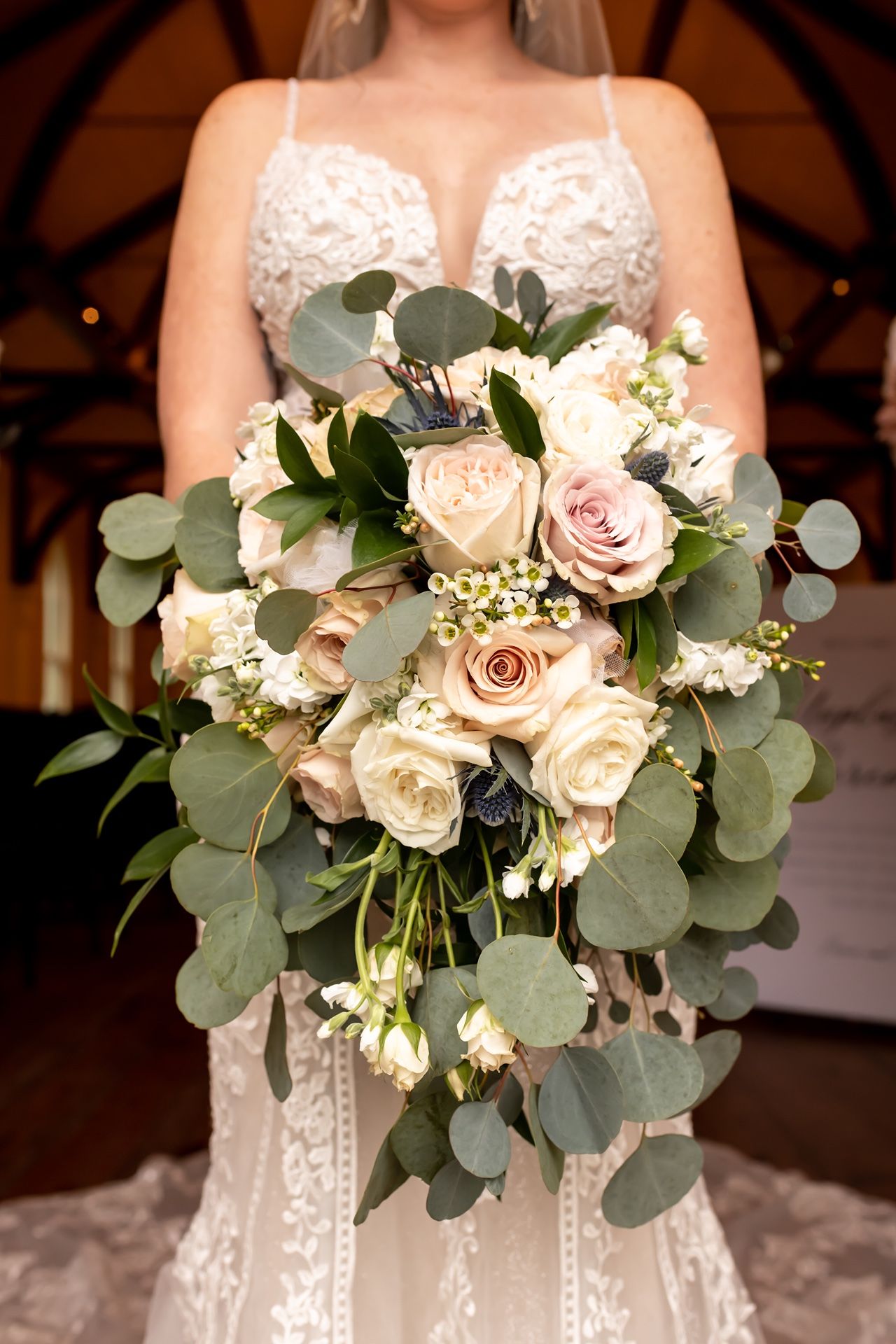 Elegant wedding bouquet features white roses, pink blooms and eucalyptus leaves against white lace dress.