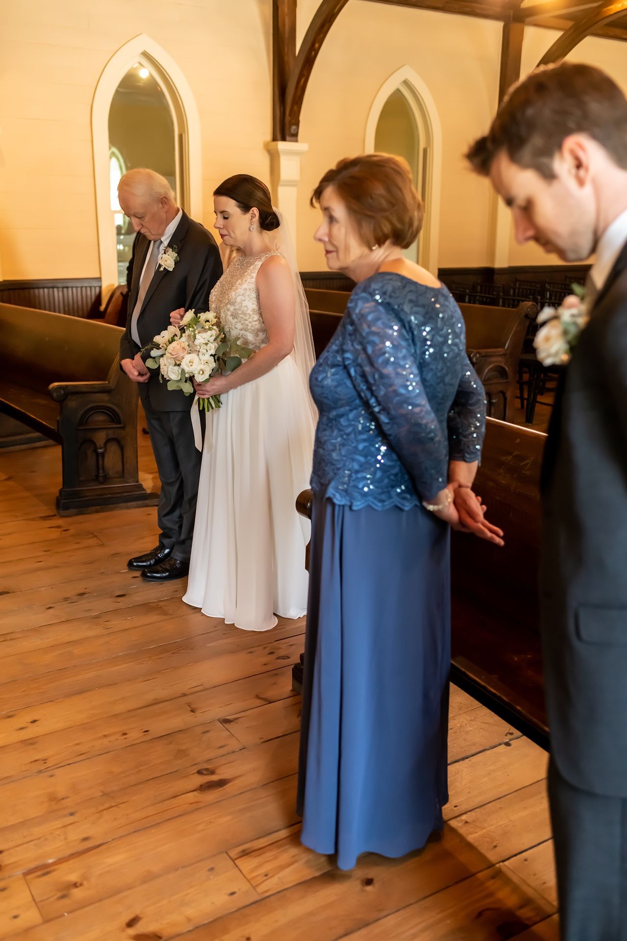 Wedding ceremony participants arranged along wooden church pews in a historic chapel.