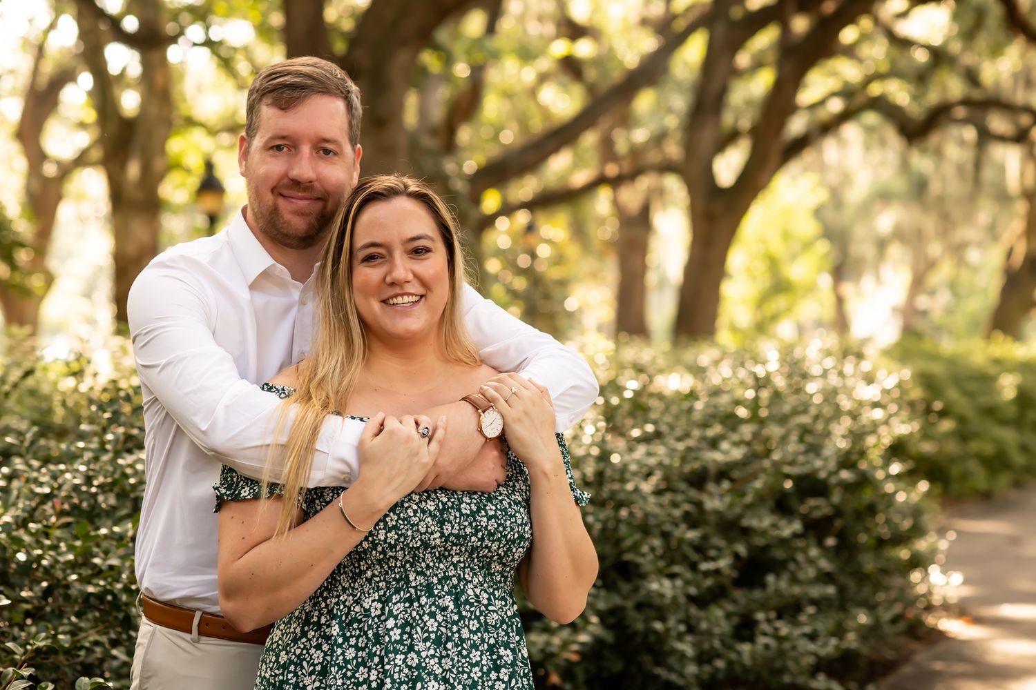 Couple embraces while walking along a tree-lined path during golden hour creating romantic outdoor portraits.
