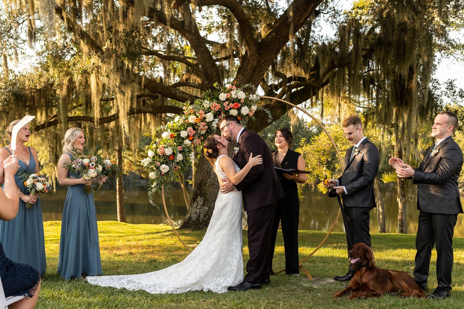 A wedding ceremony takes place under a beautiful oak tree draped with Spanish moss during golden hour.