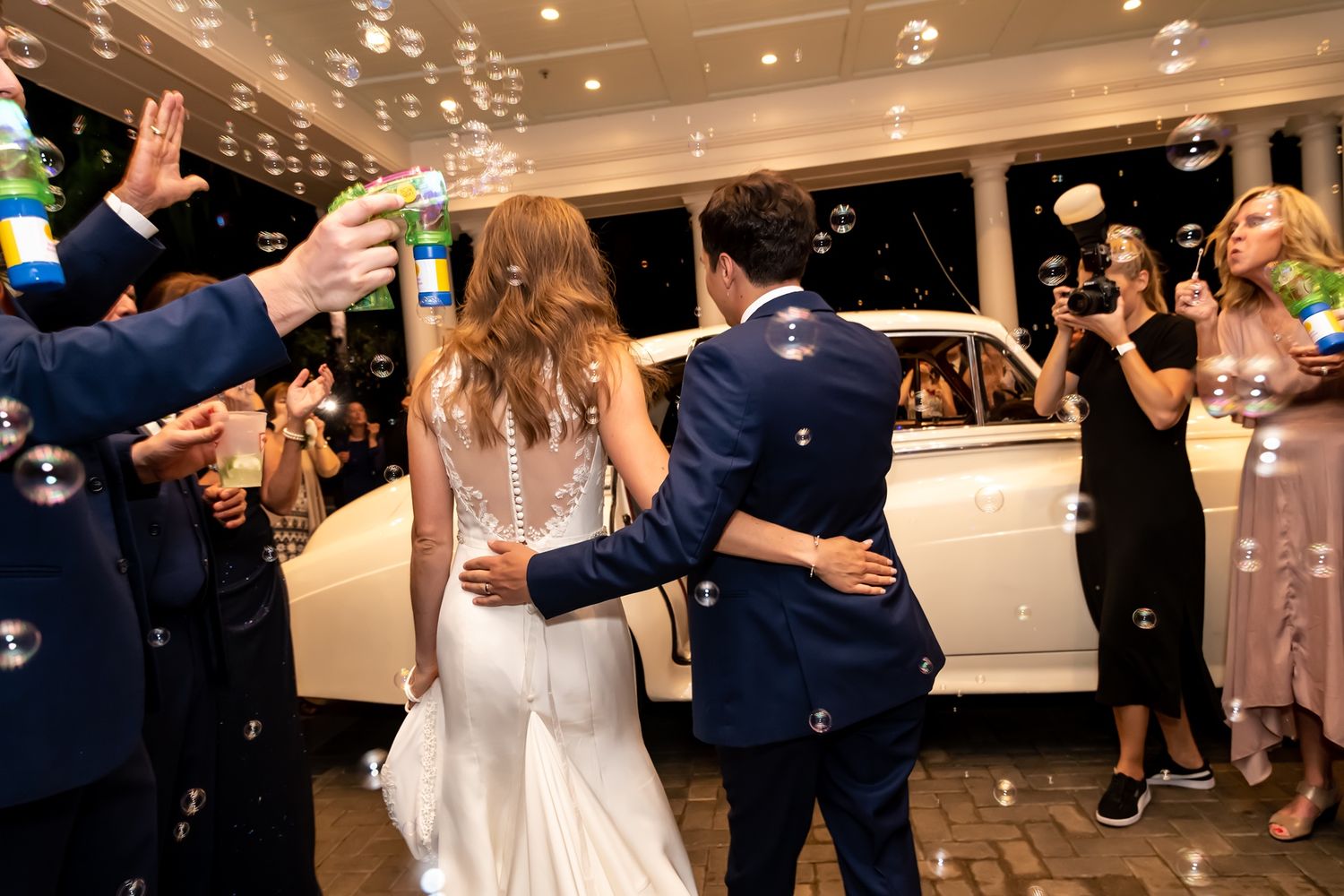 Guests blow bubbles as a couple exits their wedding reception in an elegant indoor venue.
