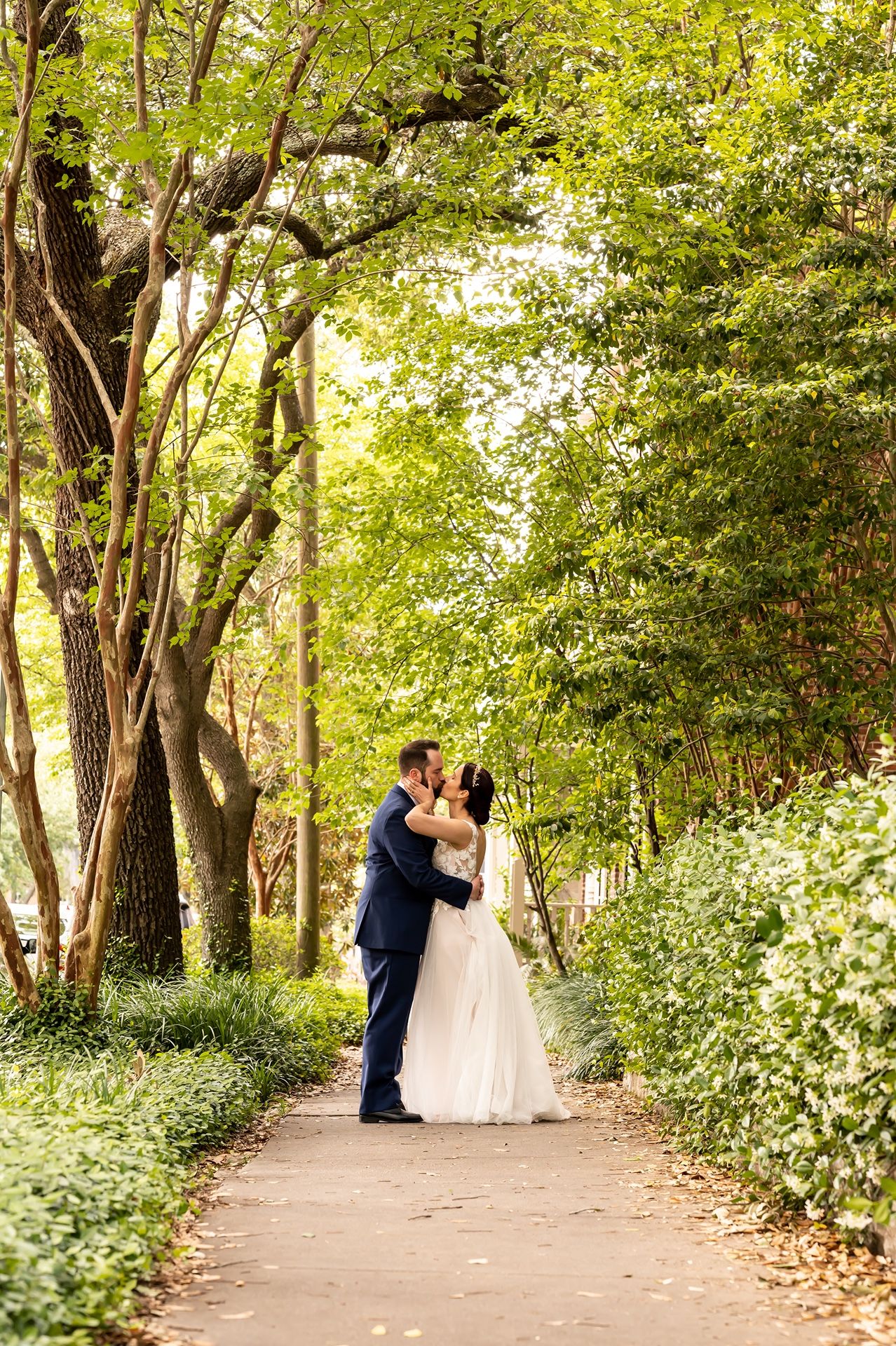 A romantic garden wedding scene on a tree-lined pathway with greenery and natural sunlight filtering through.