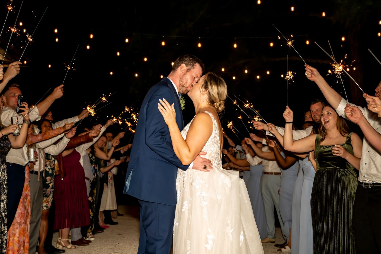 Wedding guests dance and celebrate together during a reception on the dance floor under dim lighting.