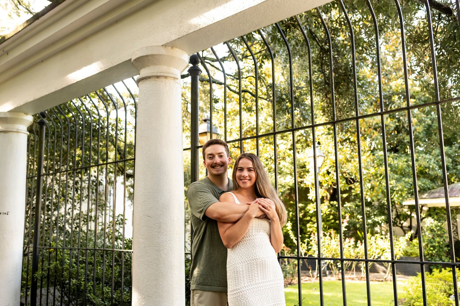 Wedding couple dances together underneath white gazebo columns during golden hour sunset lighting.