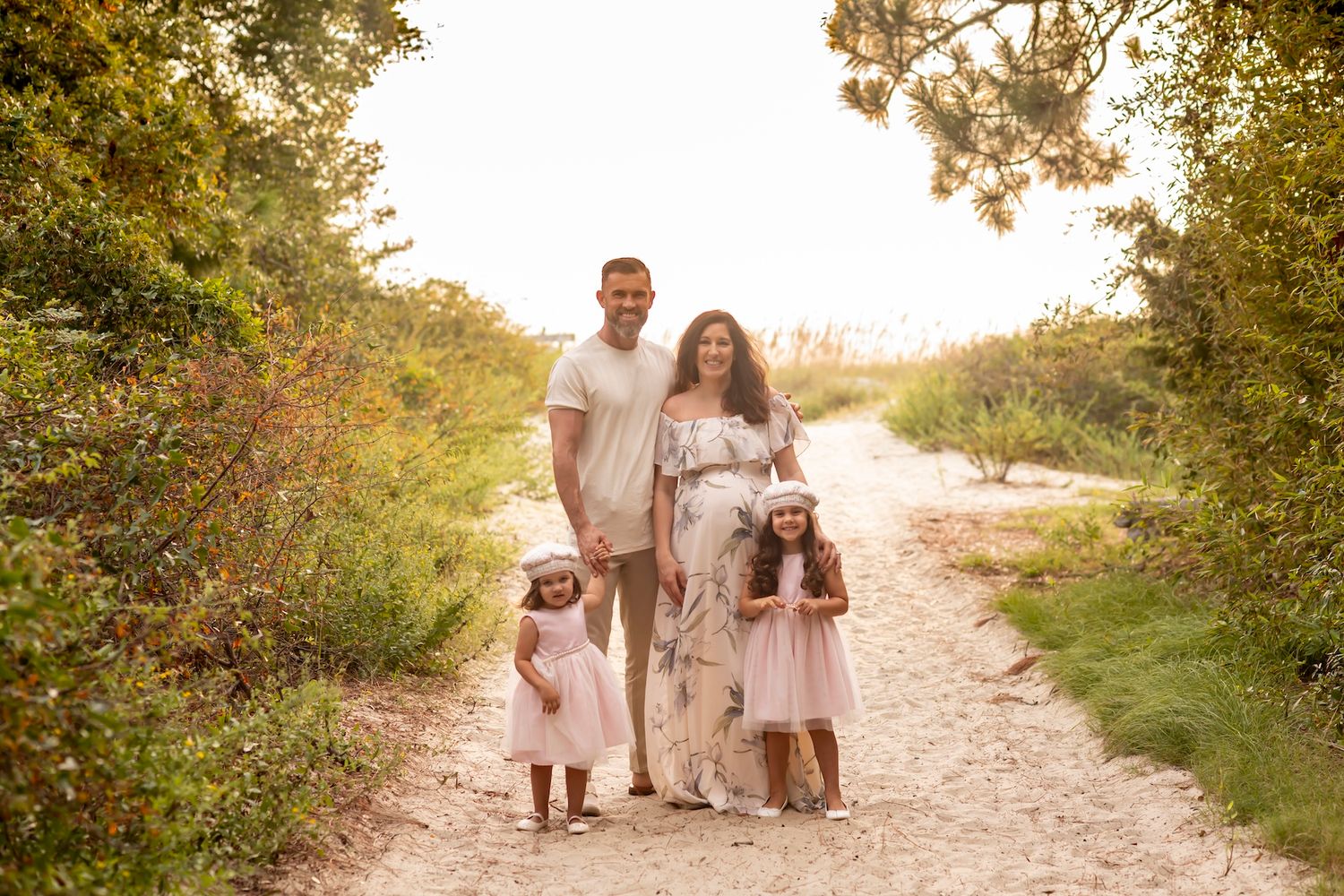Family in light colored outfits walks along a scenic sunlit nature path during golden hour sunset.
