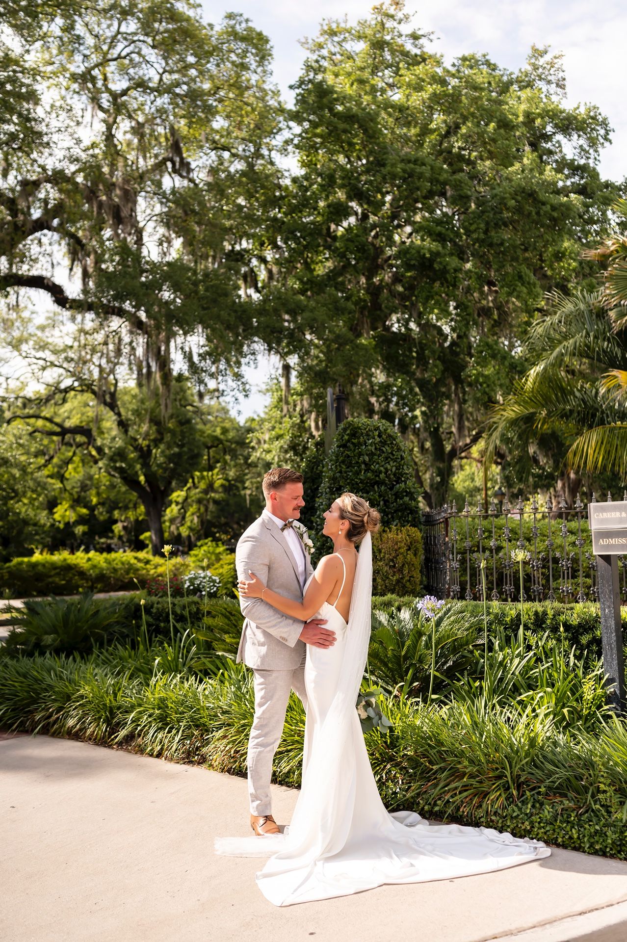 A couple shares a romantic moment in a lush garden setting with Spanish moss draped oak trees and tropical palms.
