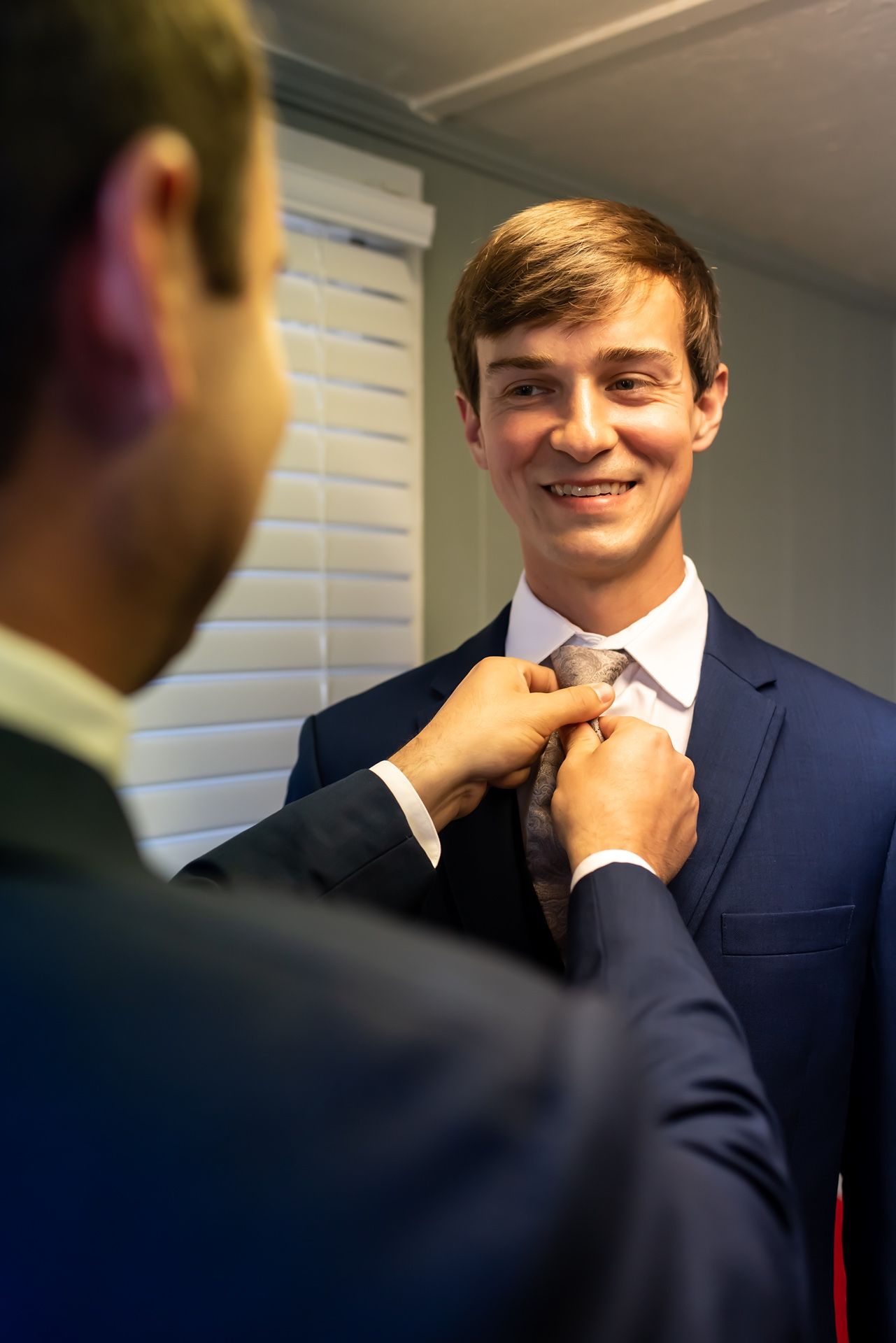 Someone helps adjust a navy blue tie on a groom before a wedding ceremony.