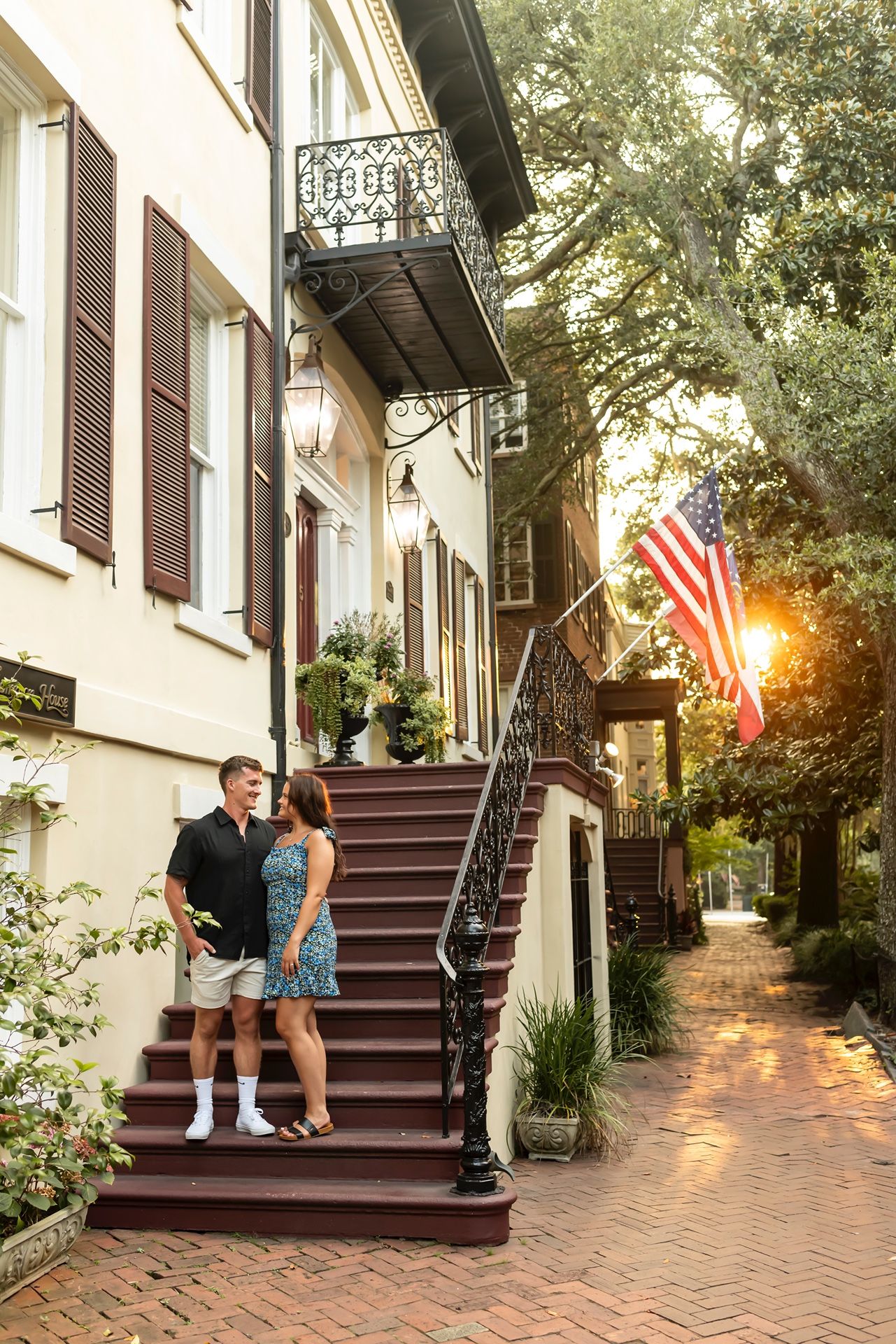 Charming historic townhouse exterior with brick sidewalk, wrought iron balcony, and American flag at sunset in Savannah.