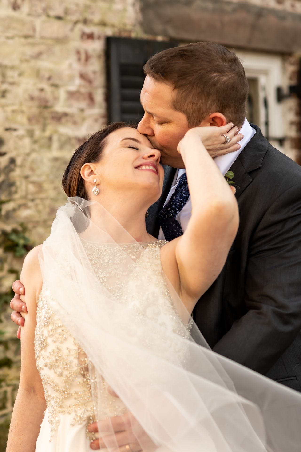 A romantic moment captured between a newlywed couple sharing a tender moment against a rustic stone wall background.