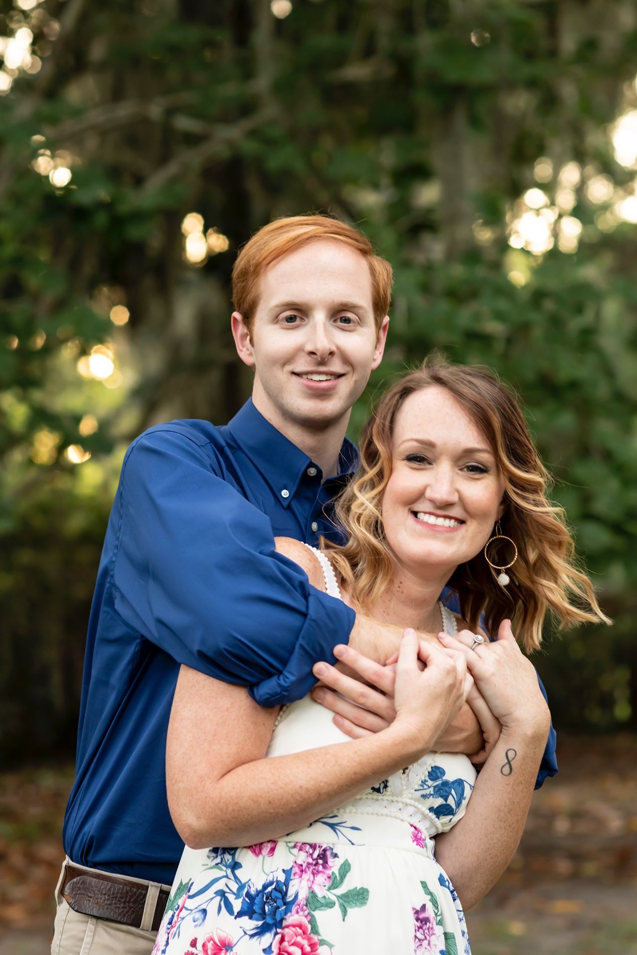 A couple embraces and dances joyfully in an outdoor setting with bokeh lights and trees in the background.