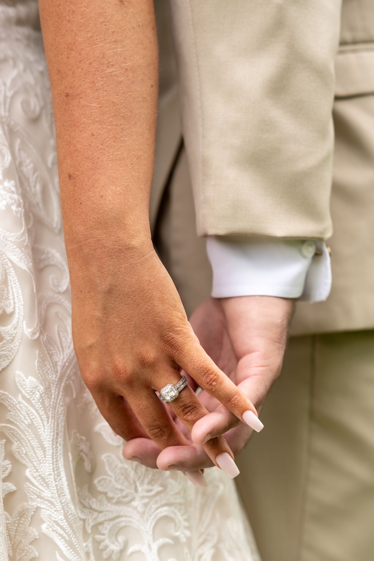 Hands holding a beautiful engagement ring against white lace fabric backdrop in natural lighting.
