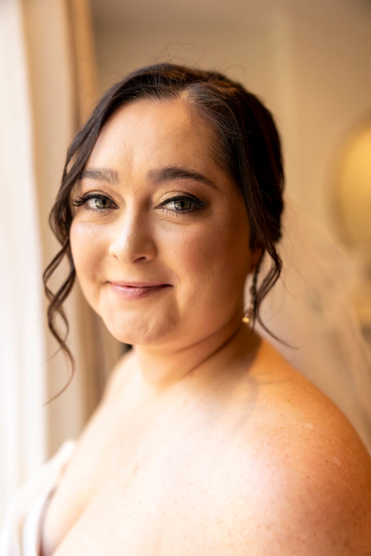 Elegant bridal portrait showing soft curls, pearl earrings and natural makeup in warm lighting.