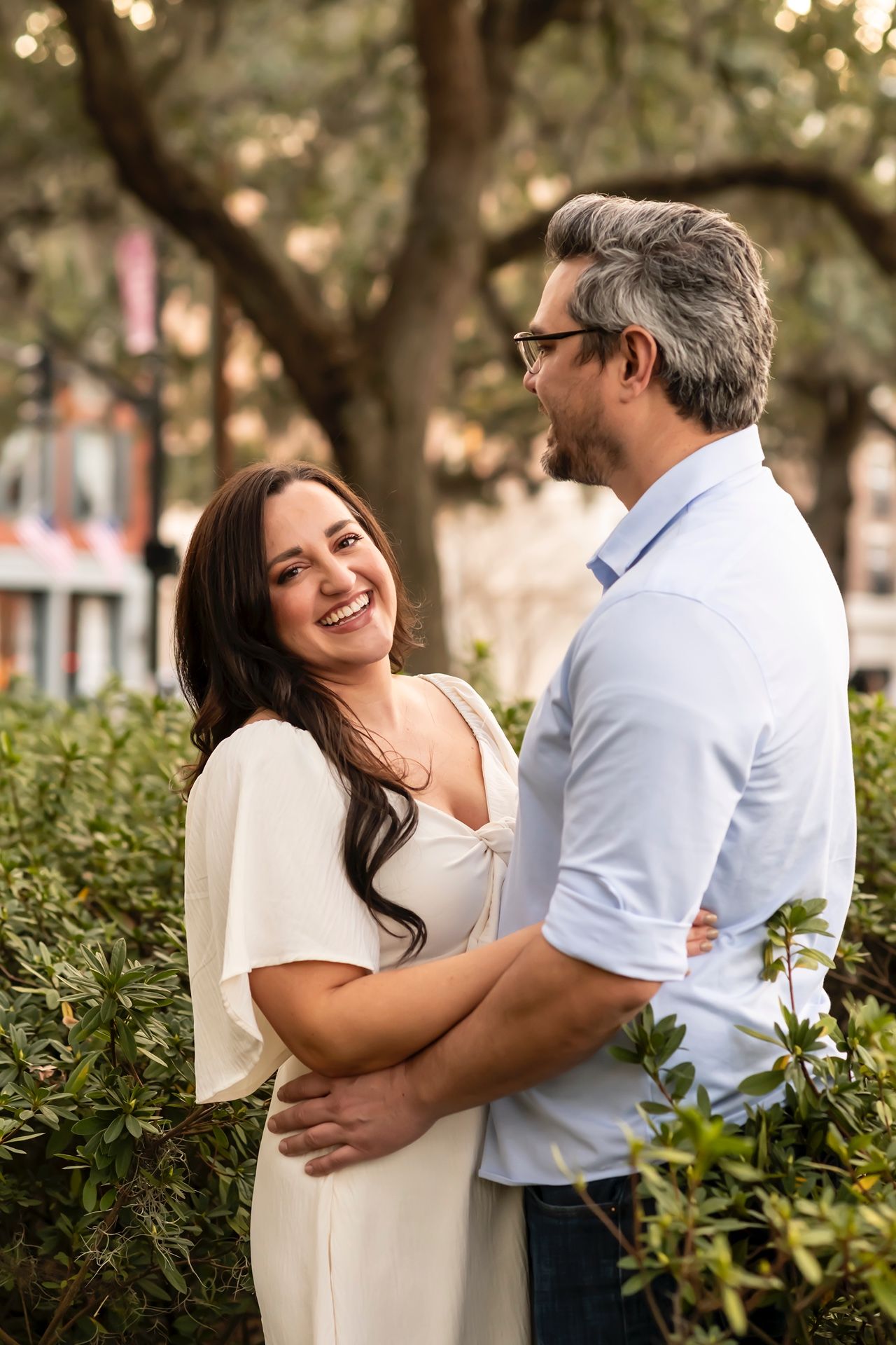 A loving couple embraces outdoors in a garden setting with bokeh lights and greenery in the background.