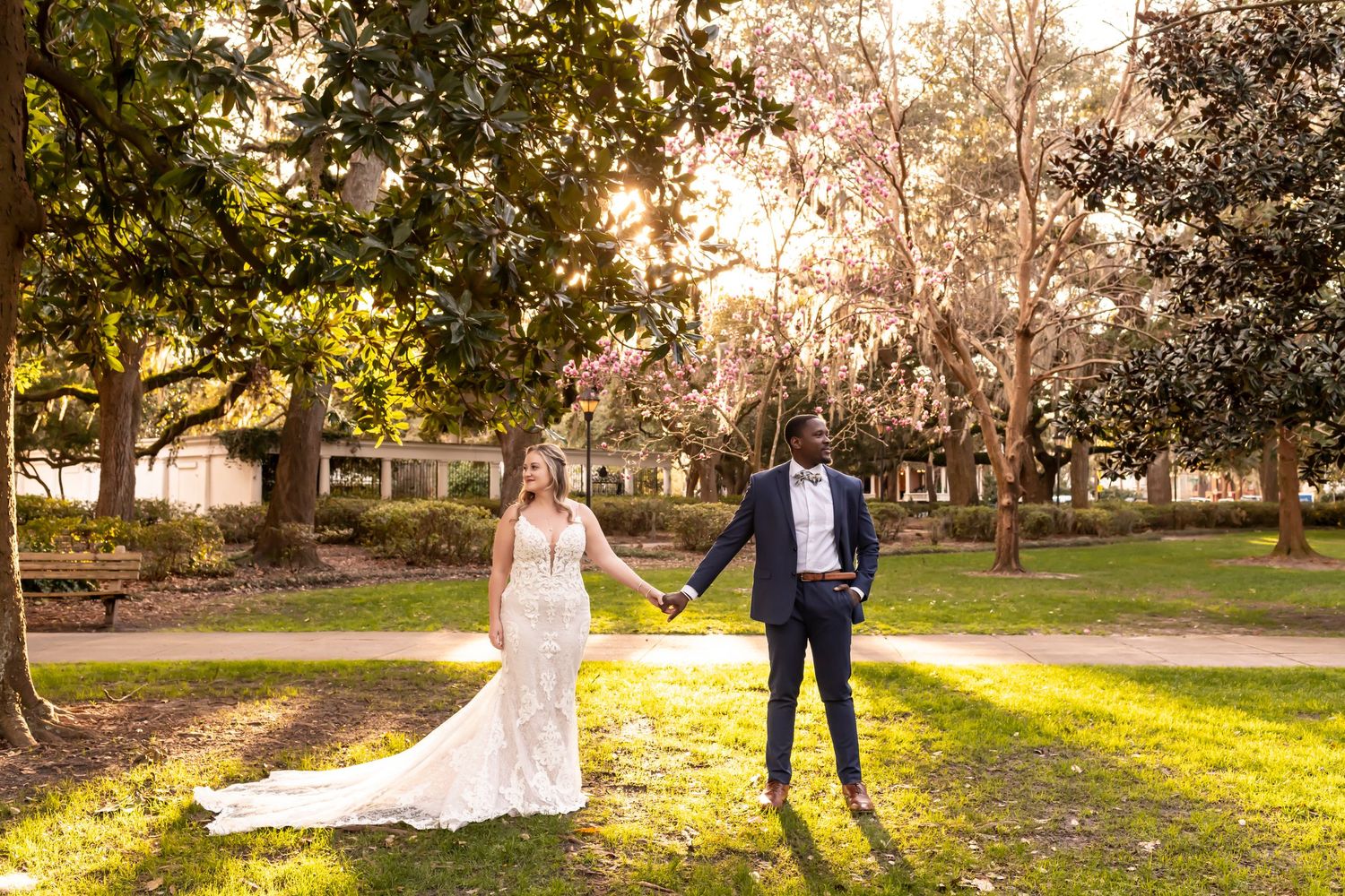 A couple poses at sunset in a park with golden sunlight filtering through trees.