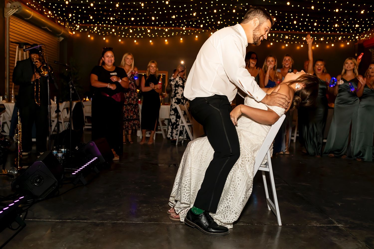 A newlywed couple performs their first dance on a dance floor under twinkling lights while guests watch.