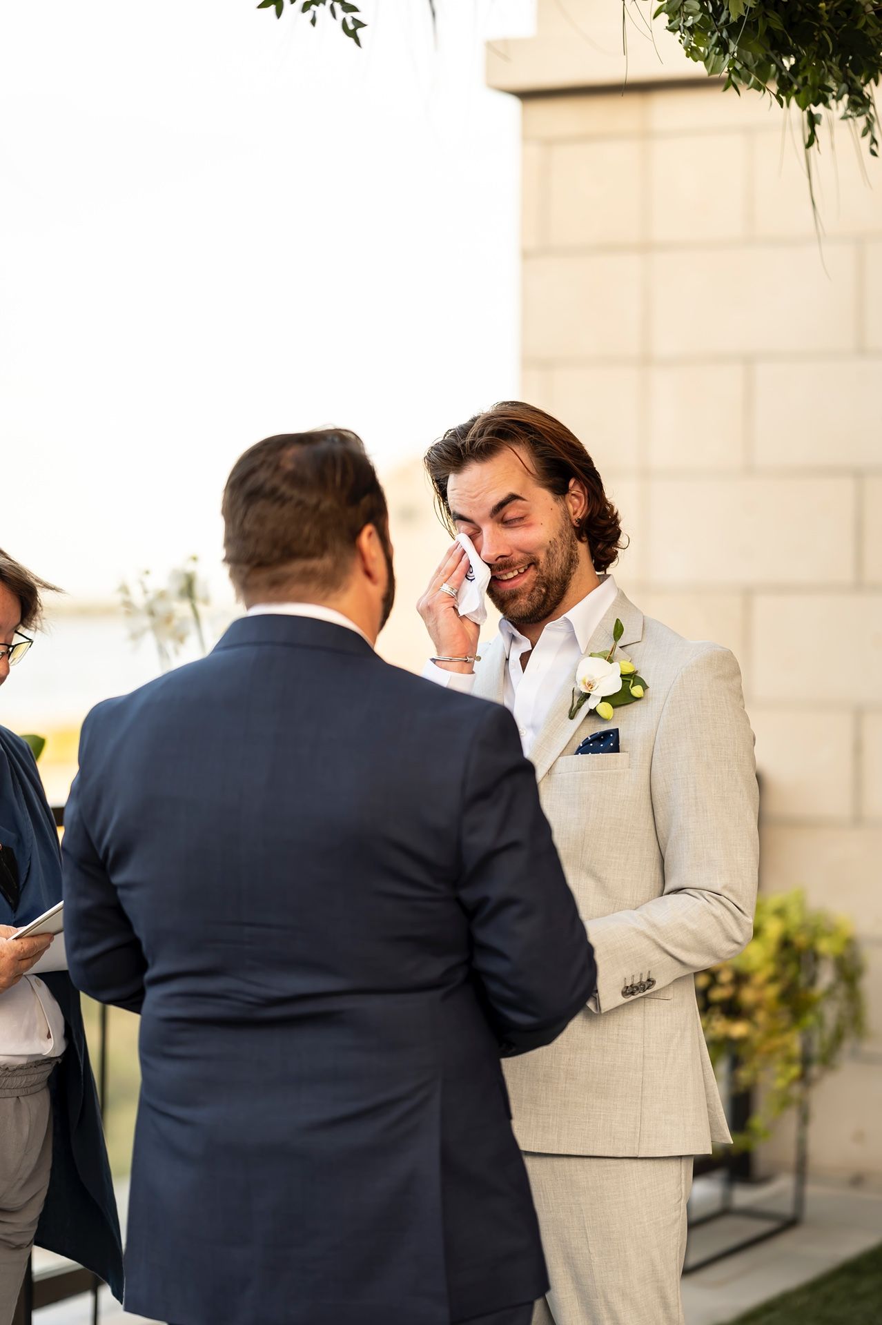 Beautiful candid moment capturing laughter and joy between wedding party members in light grey and navy blue suits.