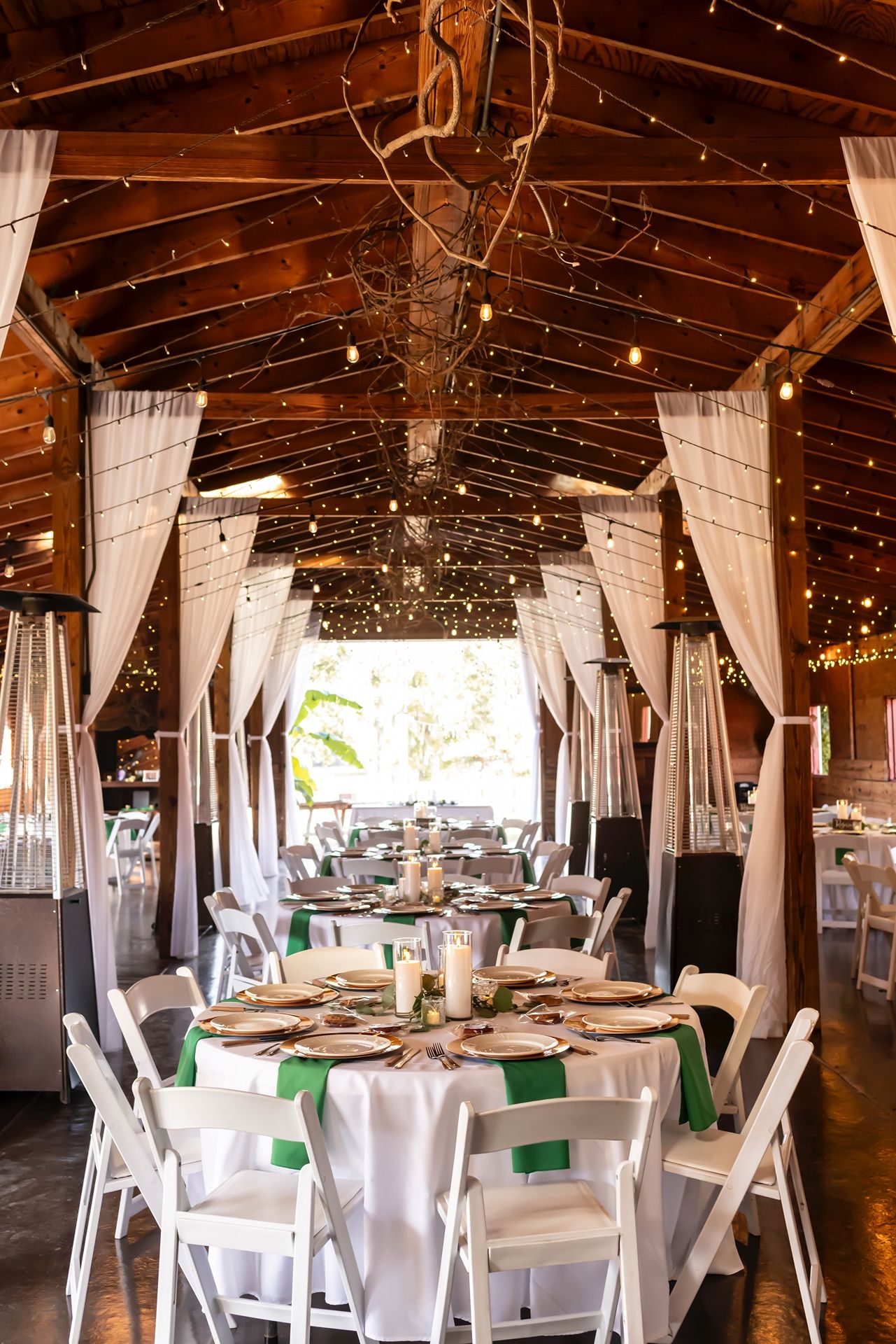 Reception venue with white table settings, hanging fabric drapes and twinkling string lights in a rustic barn interior.
